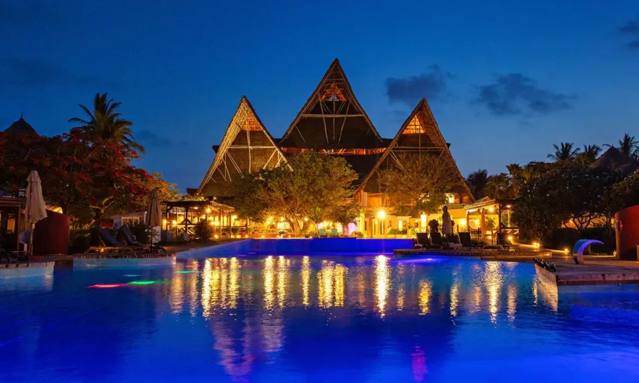 Essque Zalu Zanzibar's lagoon-style pool lit at night beneath its triple Makuti-thatched roof