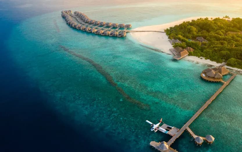 Aerial view of JA Manafaru's overwater villas and a seaplane at the jetty at sunset, Haa Alifu Atoll, Maldives