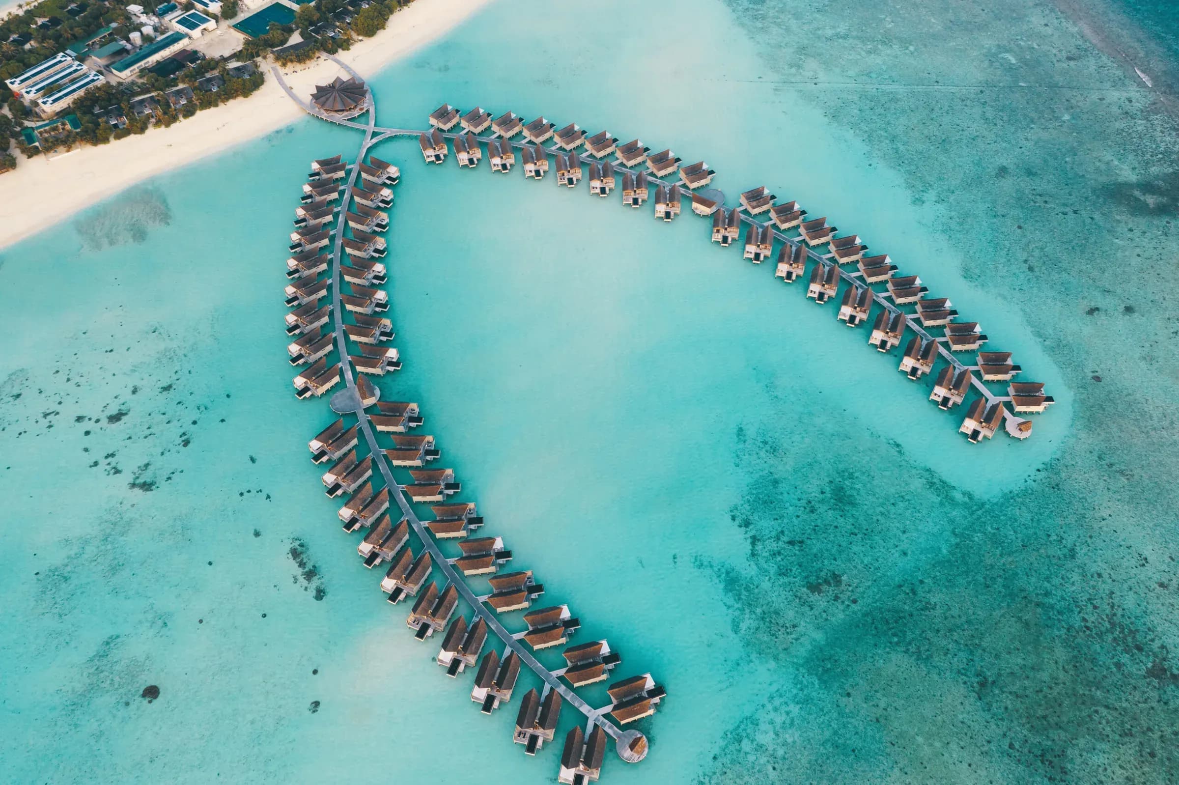 Aerial view of Kuredhivaru Resort and Spa's overwater villa jetties over the turquoise lagoon, Noonu Atoll, Maldives