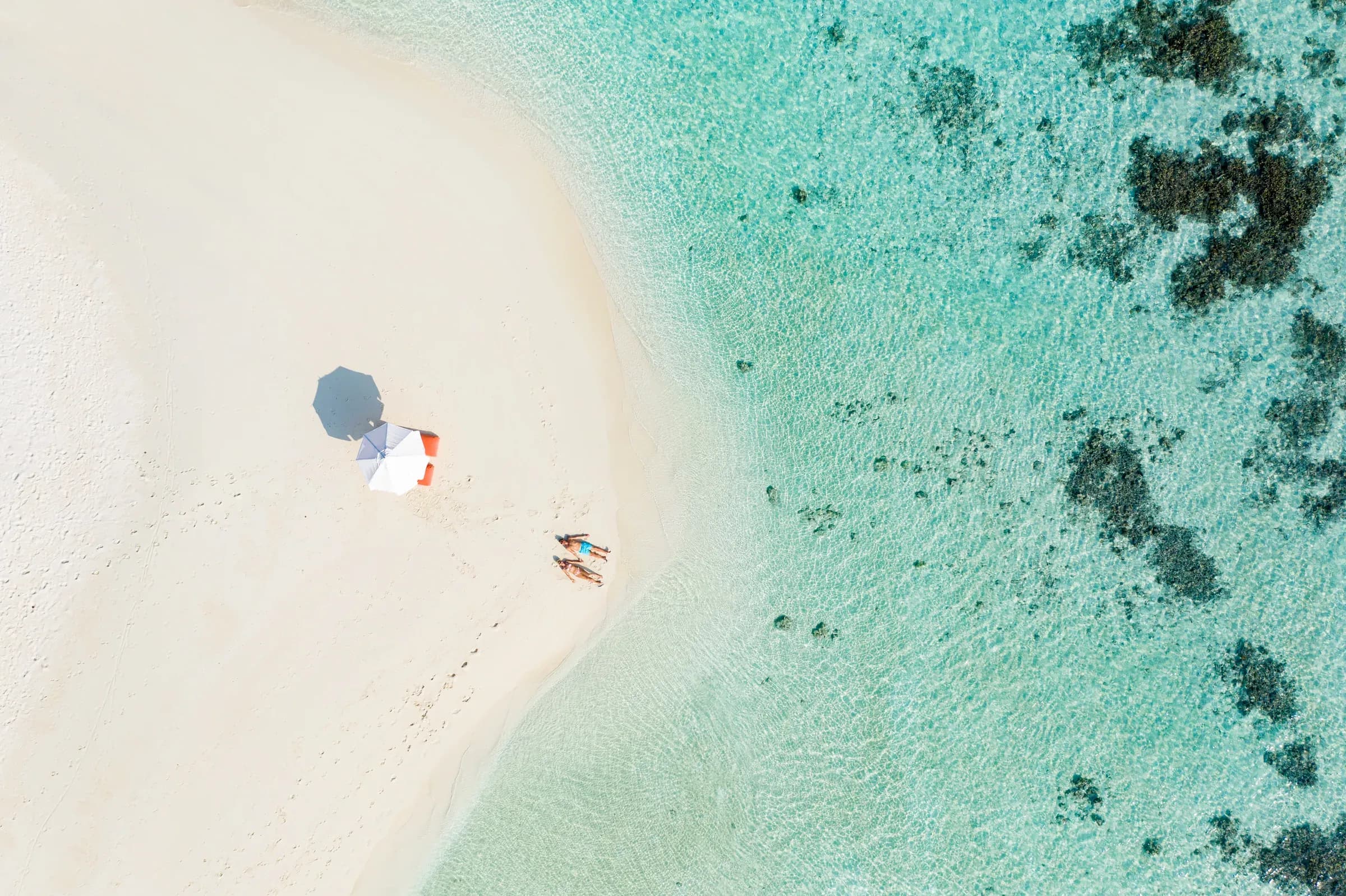 Aerial view of a lone beach umbrella and sunbathers on the white sand beach at V Villas Maldives at Mirihi, South Ari Atoll
