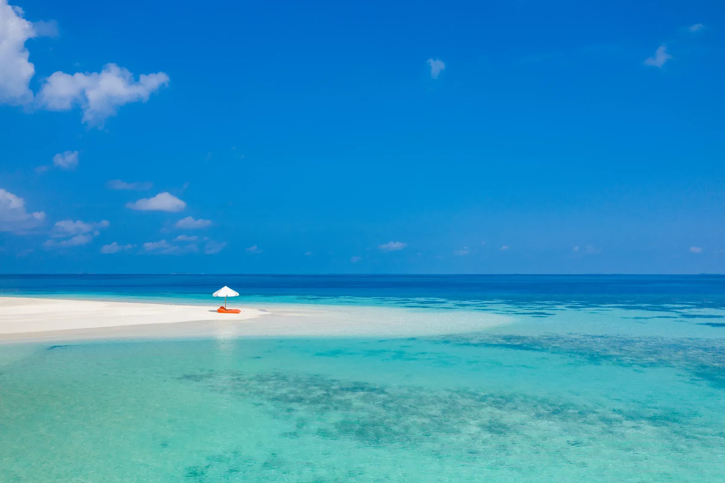 A single beach umbrella on a narrow white sandbank surrounded by turquoise water at V Villas Maldives at Mirihi