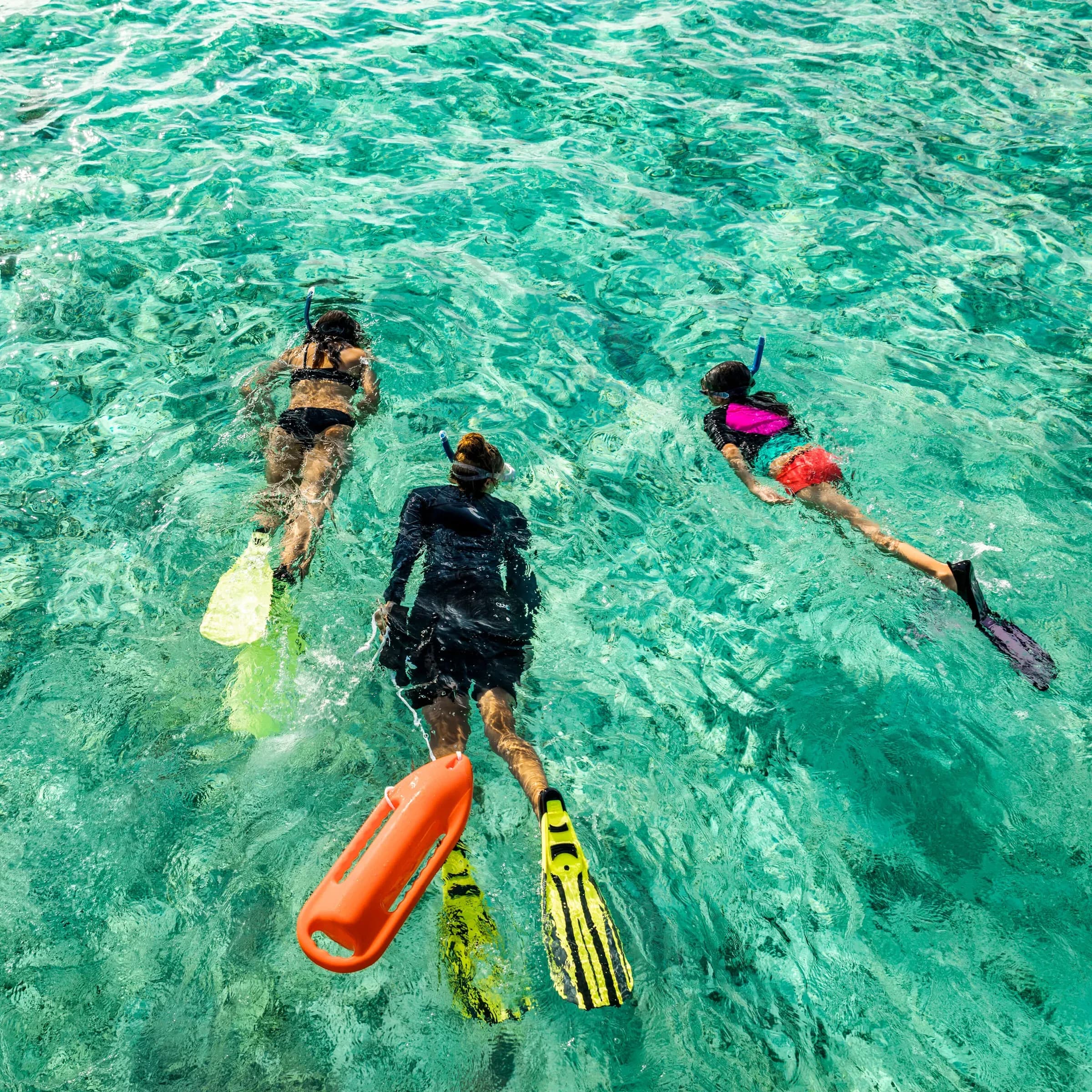 Family snorkelling together in clear lagoon water at COMO Maalifushi