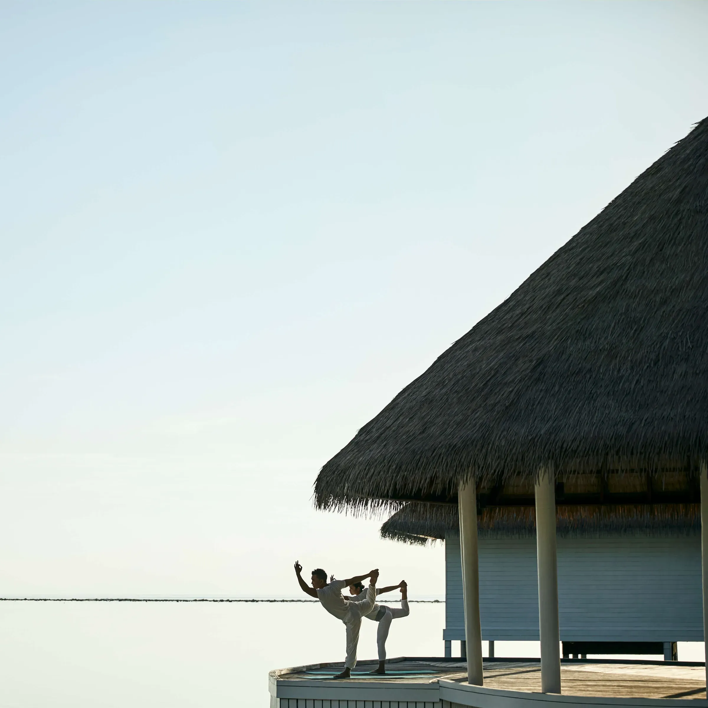 Couple practising yoga on an overwater deck at COMO Shambhala, COMO Maalifushi