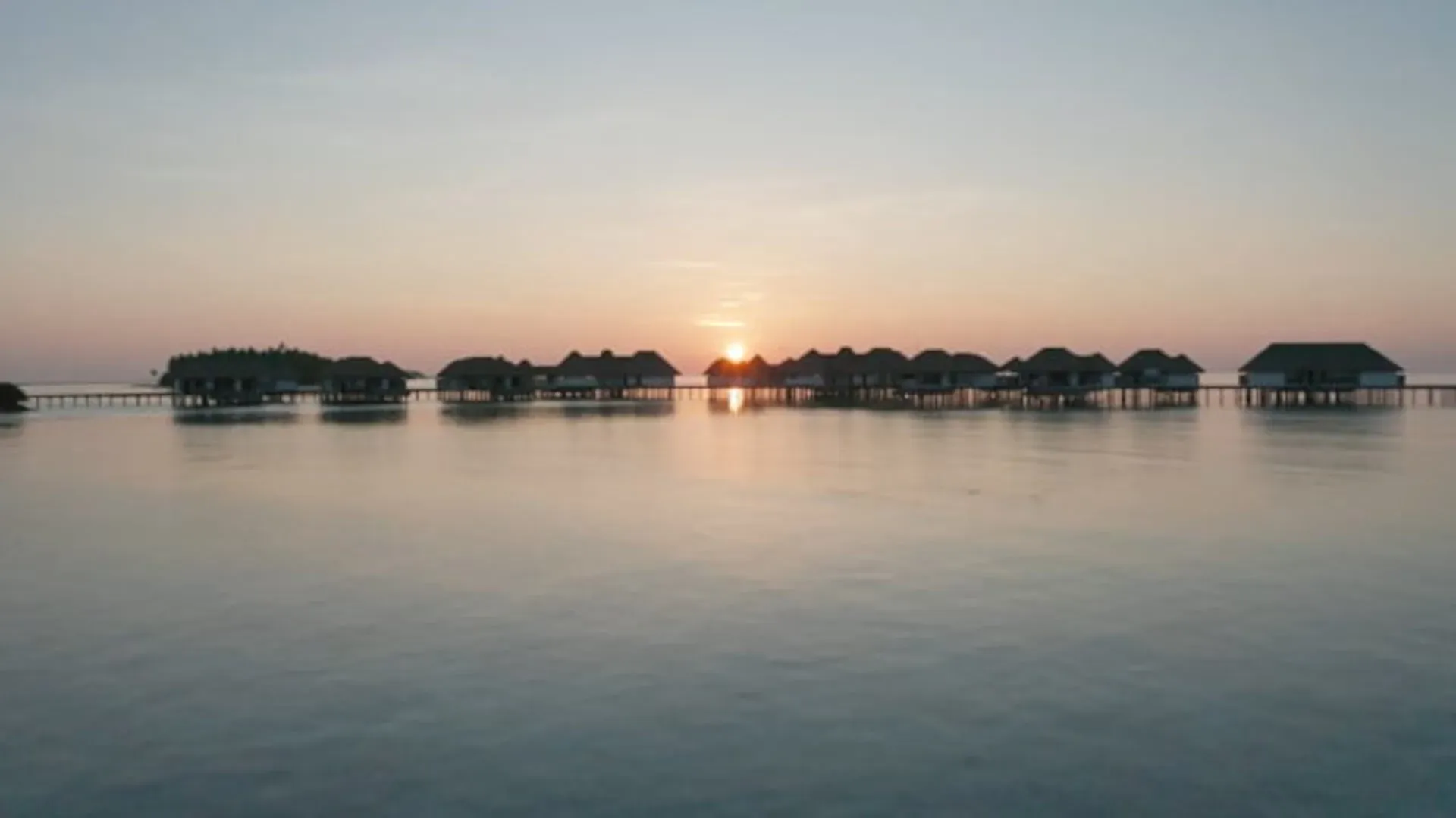 Overwater villas at sunset with the sun setting behind the jetty, COMO Maalifushi, Thaa Atoll