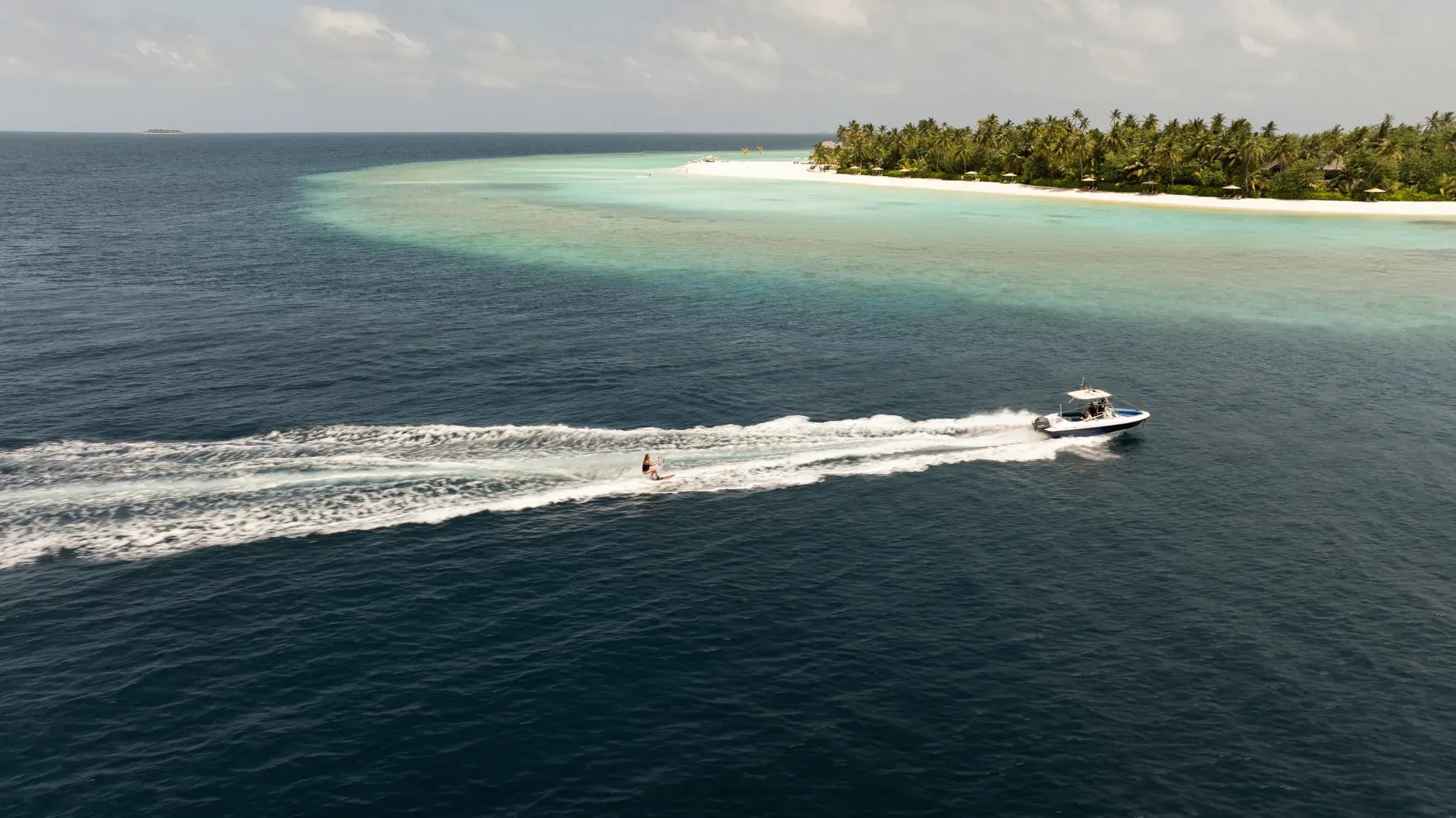 Speedboat and wakeboarder passing Constance Halaveli's beach and lagoon in the North Ari Atoll, Maldives