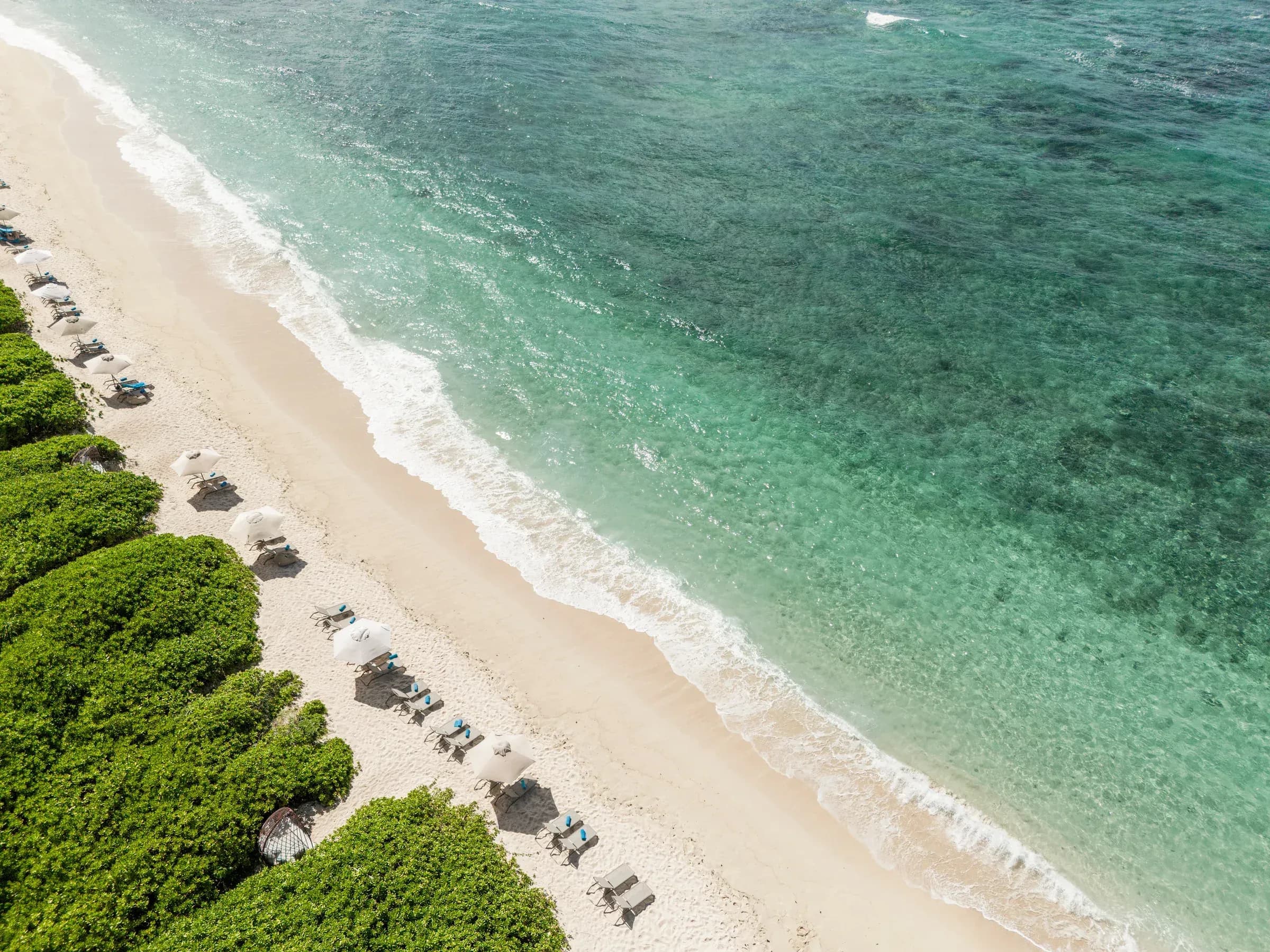 Aerial view of the beach at Constance Le Chaland, sun loungers under thatched parasols beside a turquoise lagoon, Mauritius