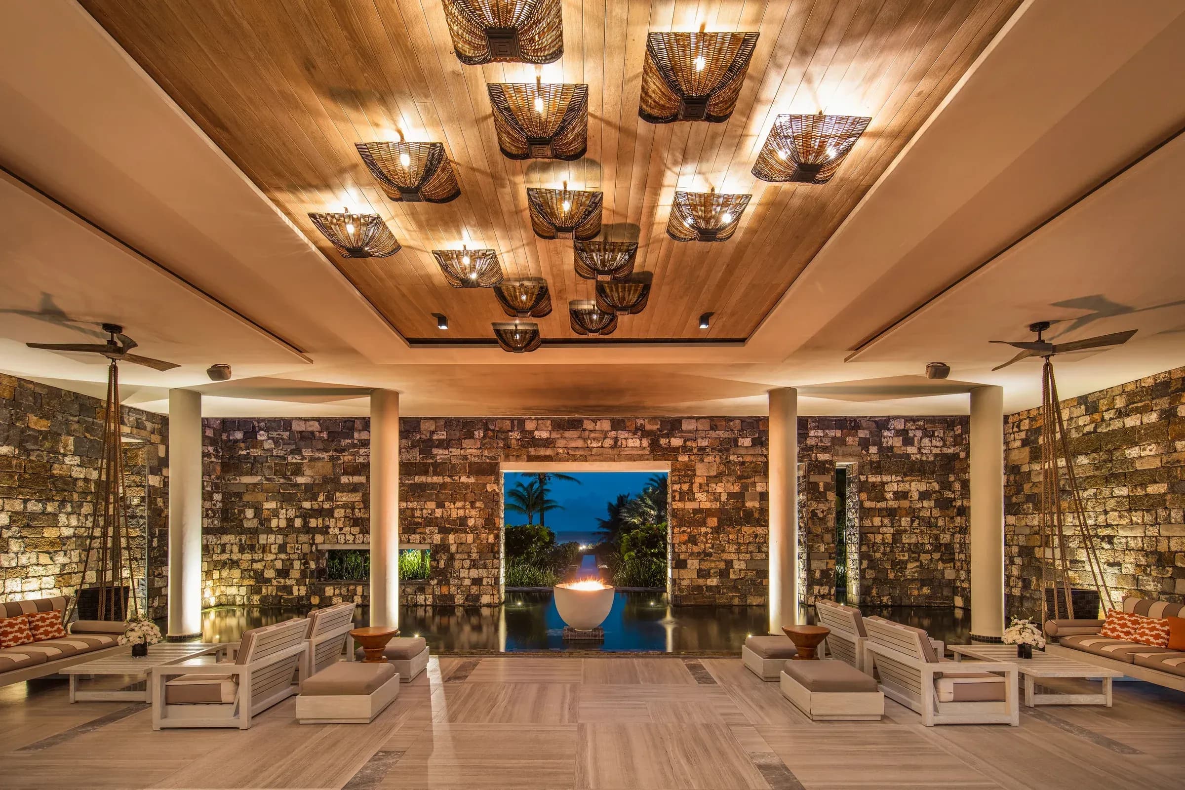Lounge and lobby at dusk at Constance Le Chaland, stone walls and a raised firepit reflecting in a still pool