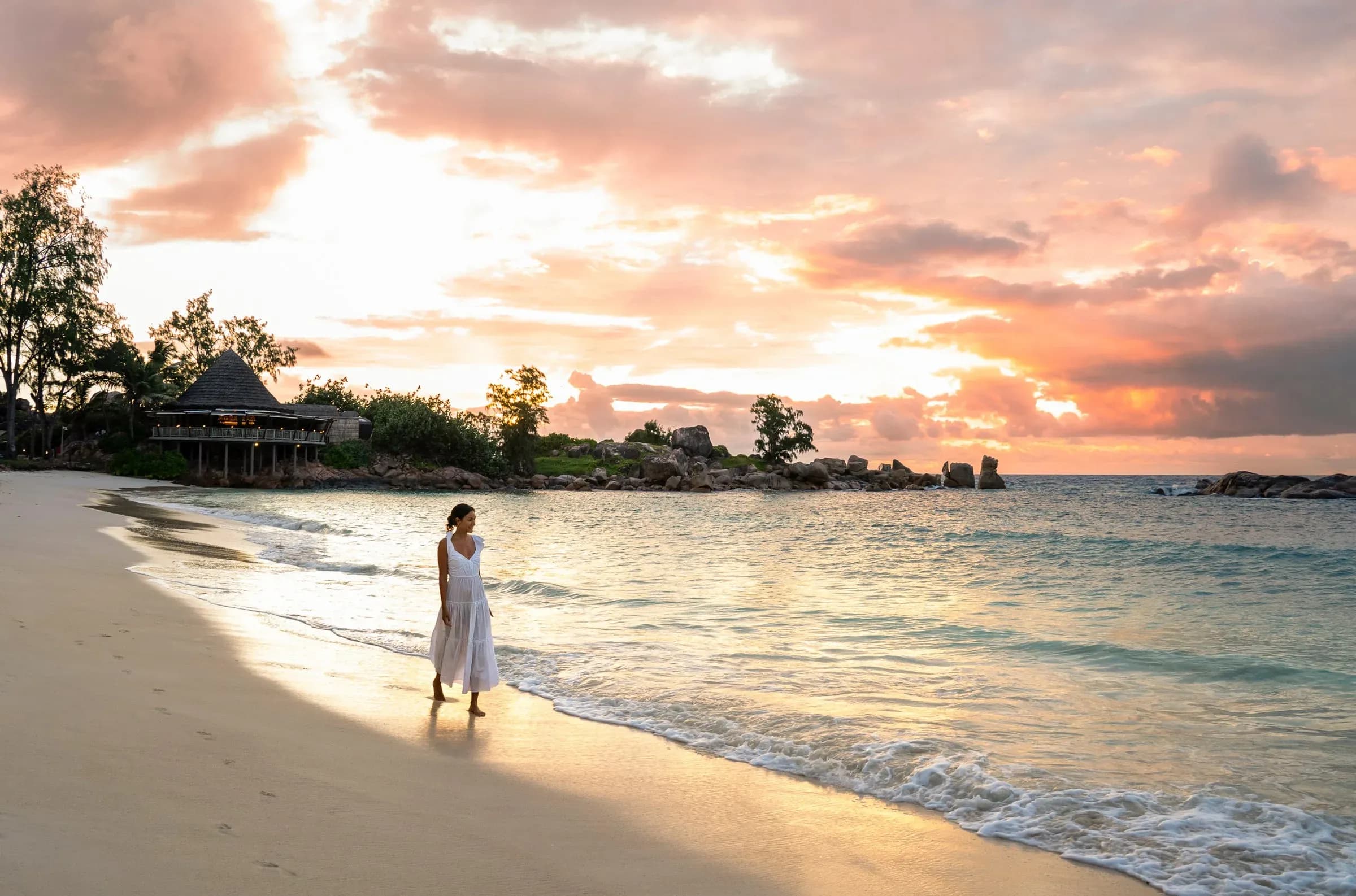 Guest walking along the beach at sunset in front of The Nest restaurant at Constance Lemuria
