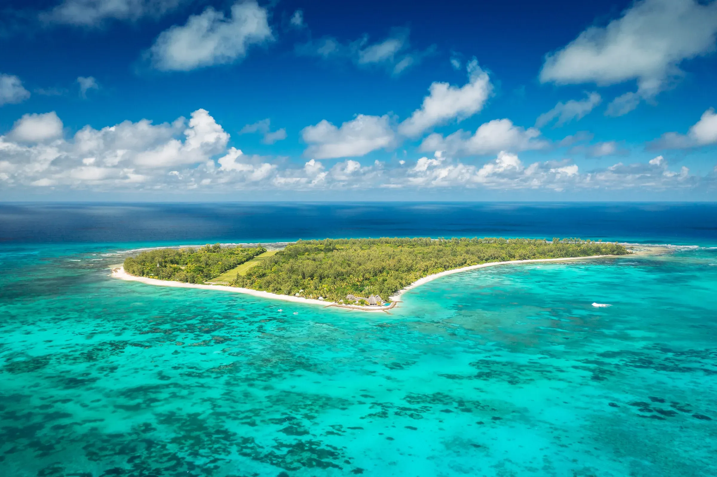 Aerial view of the whole of Denis Private Island, showing its forested interior ringed by reef and white sand