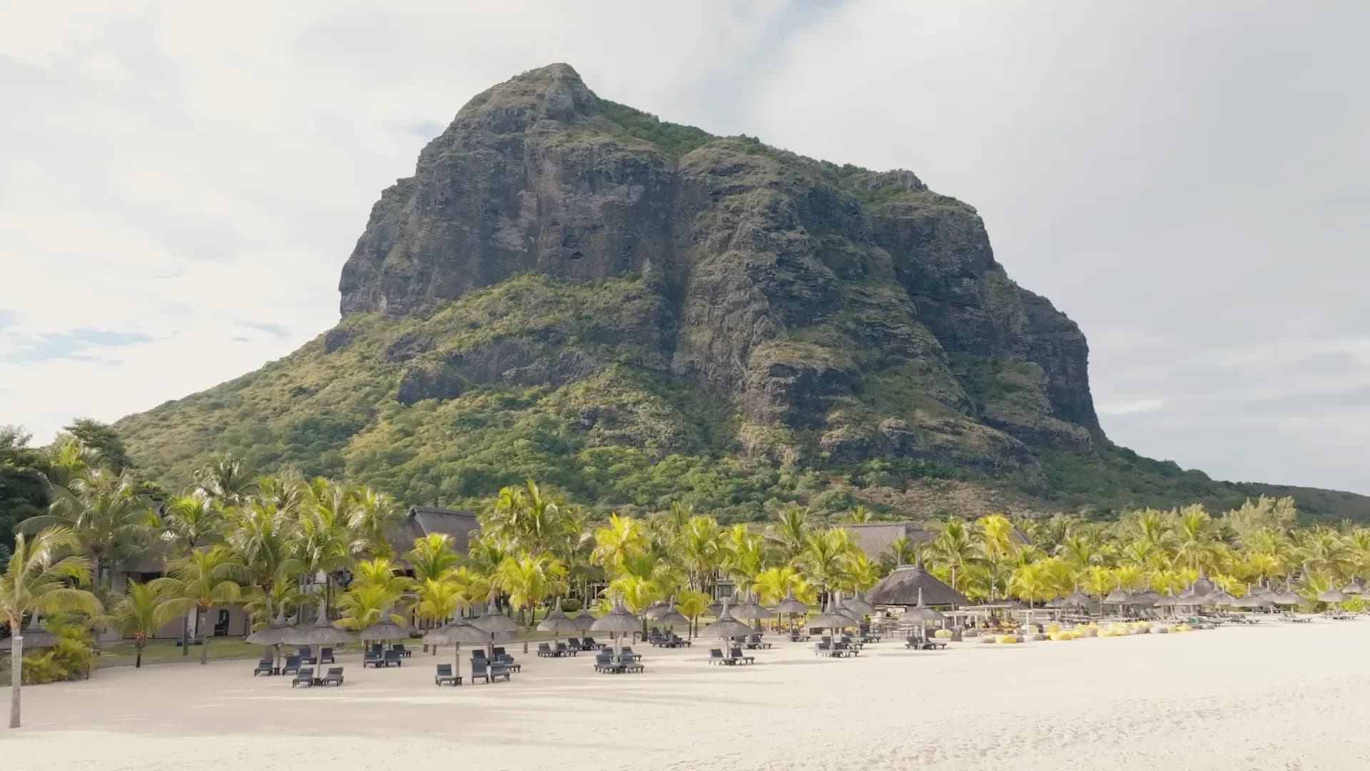Le Morne Brabant mountain rising behind the beach and sun loungers at Dinarobin Beachcomber Golf Resort & Spa, Mauritius