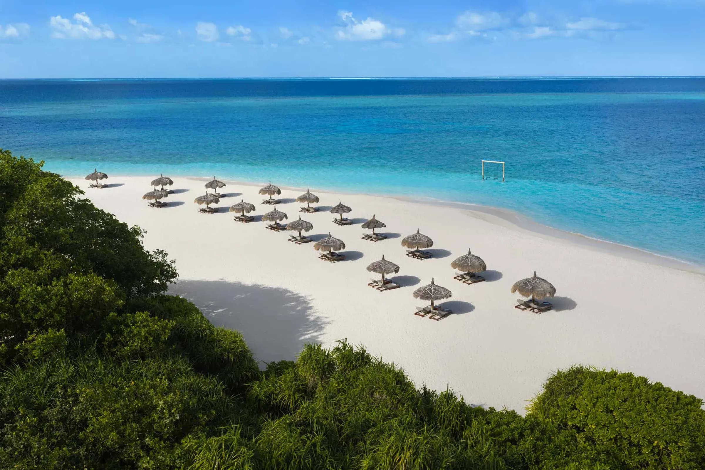 Aerial view of straw-thatched beach umbrellas along the white sand and turquoise lagoon at Emerald Maldives Resort & Spa