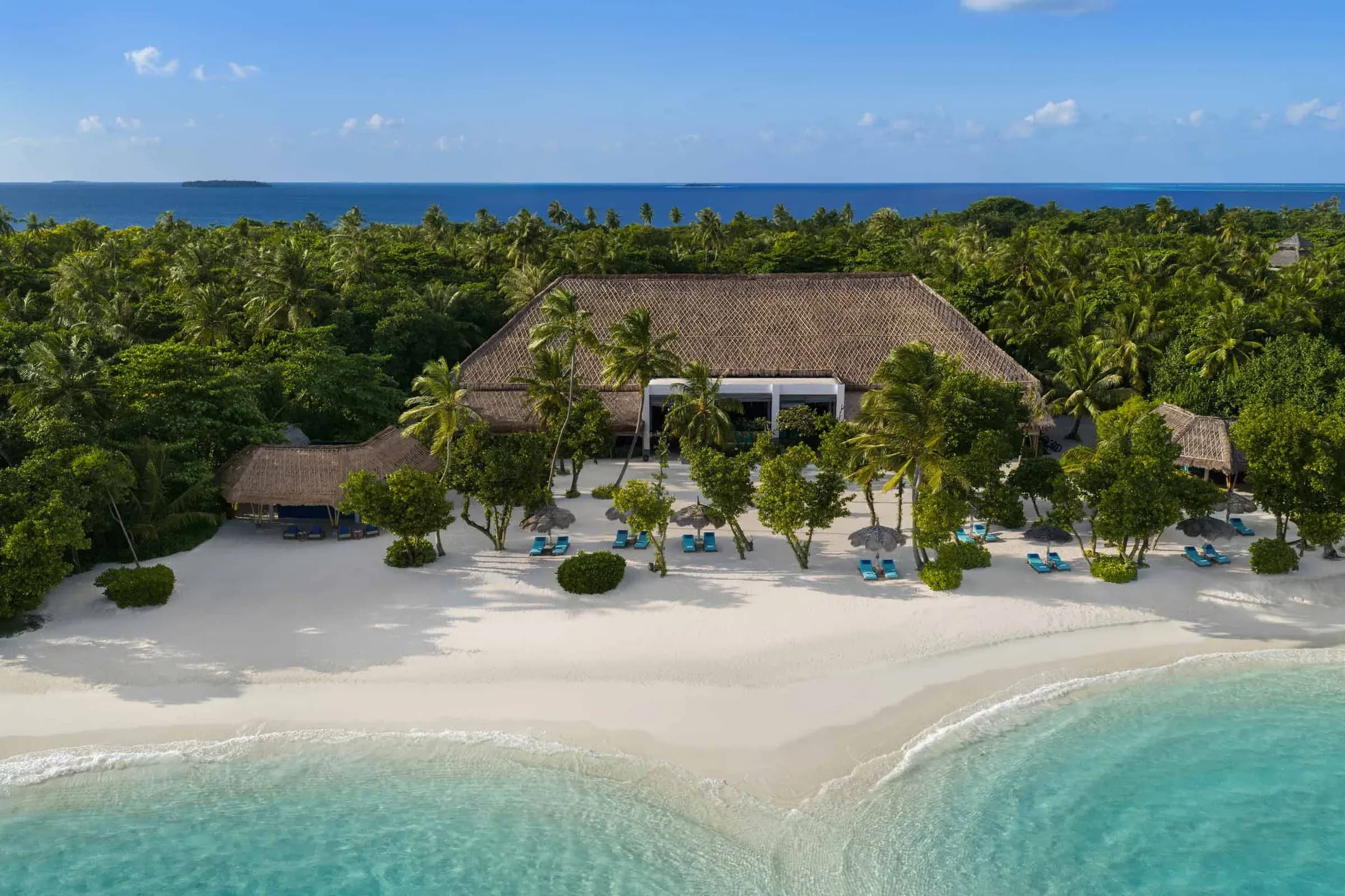 Beachfront restaurant pavilion framed by palm trees at Emerald Maldives Resort & Spa, Raa Atoll
