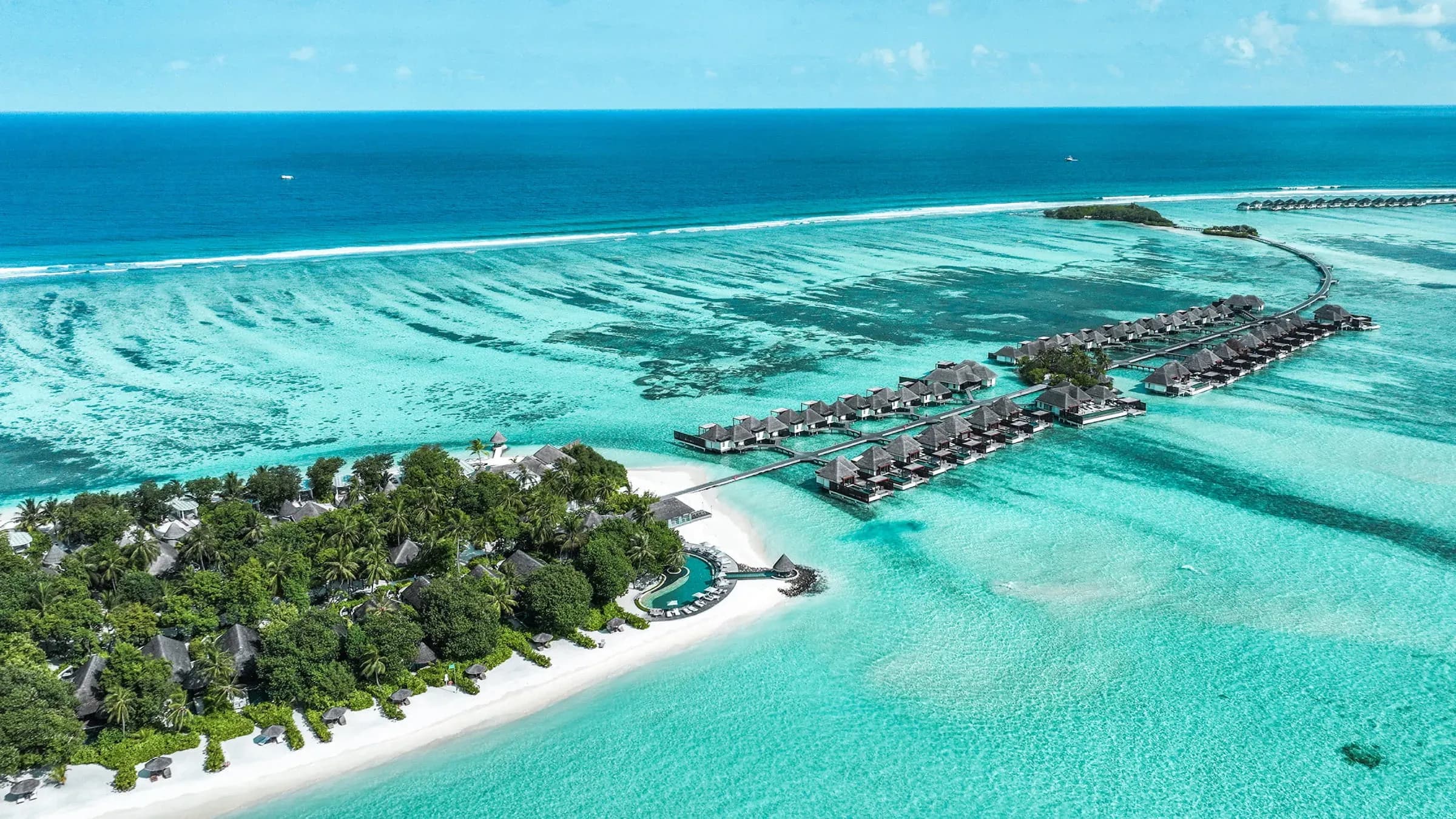 Aerial view of Four Seasons Resort Maldives at Kuda Huraa, showing overwater villas over the reef and the beach island