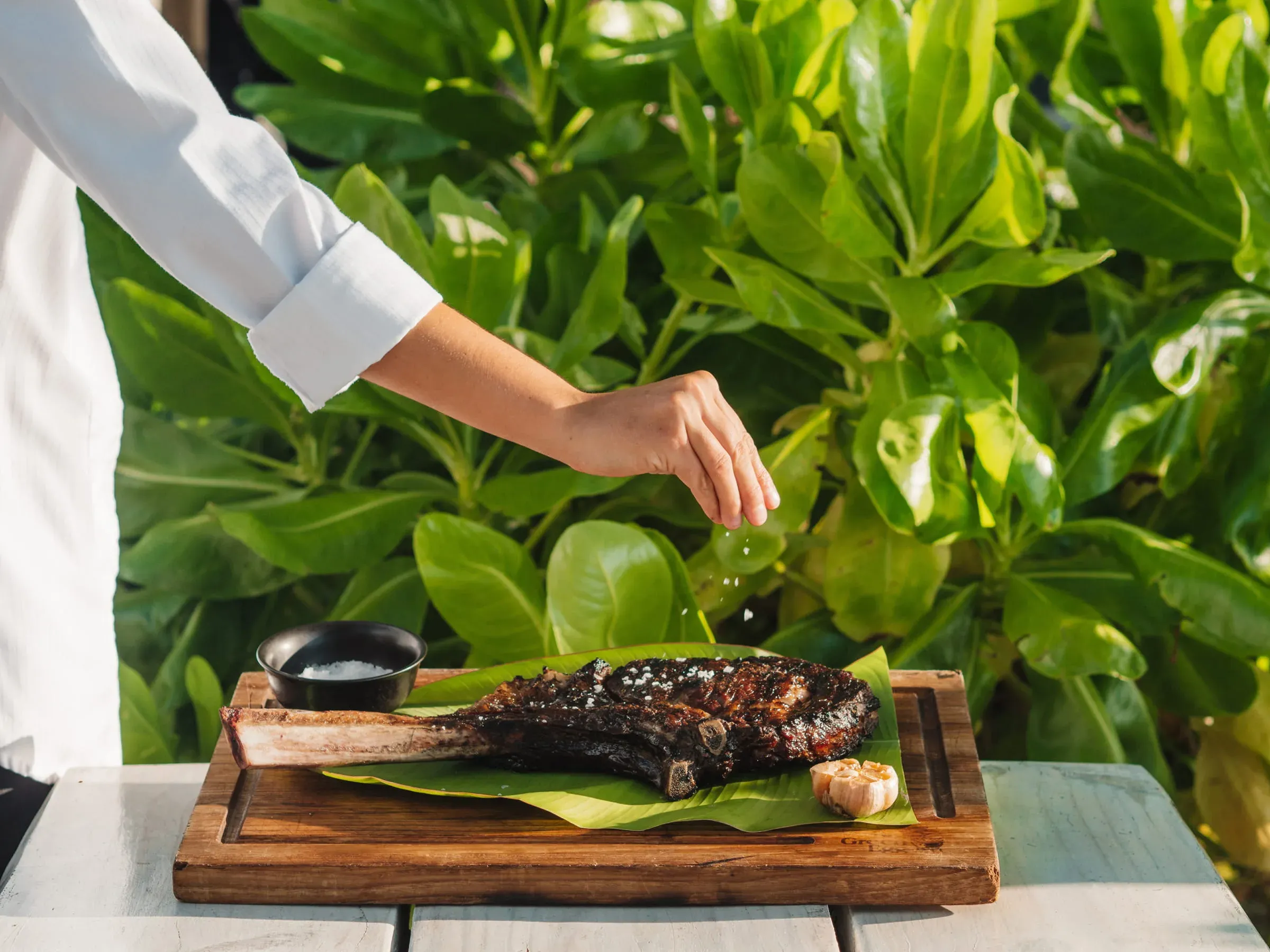 Chef seasoning a grilled tomahawk rib-eye steak on a banana leaf at Steak Shack, Four Seasons Resort Seychelles