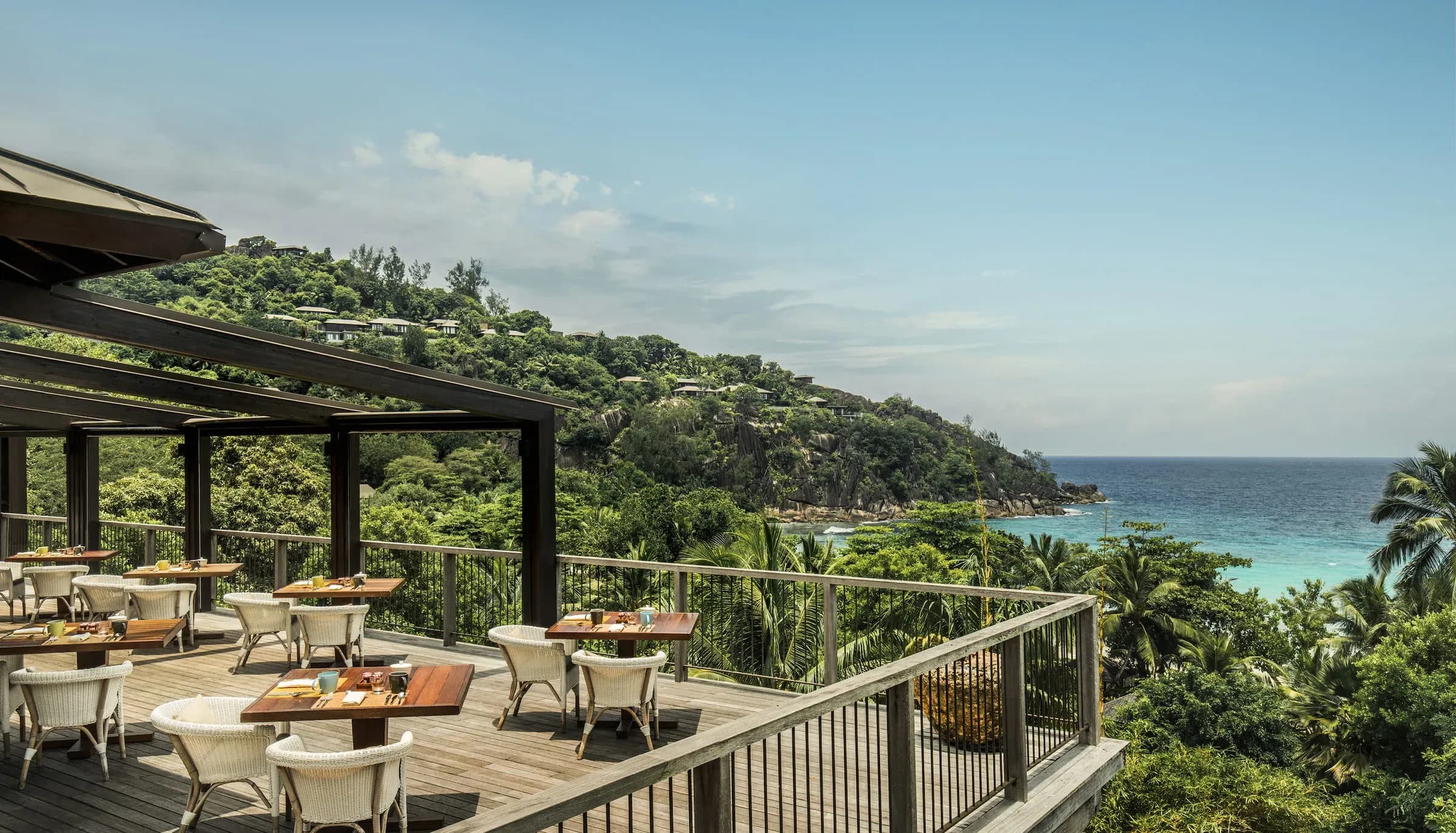 ZEZ's outdoor dining room on a wood deck overlooking palm trees and blue sky at Four Seasons Resort Seychelles