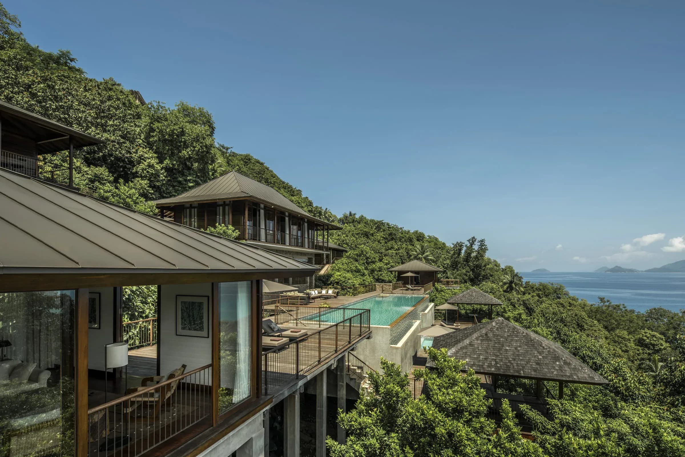 Four-Bedroom Residence Villa rooftops and patios among trees on the mountainside, ocean below, Four Seasons Resort Seychelles