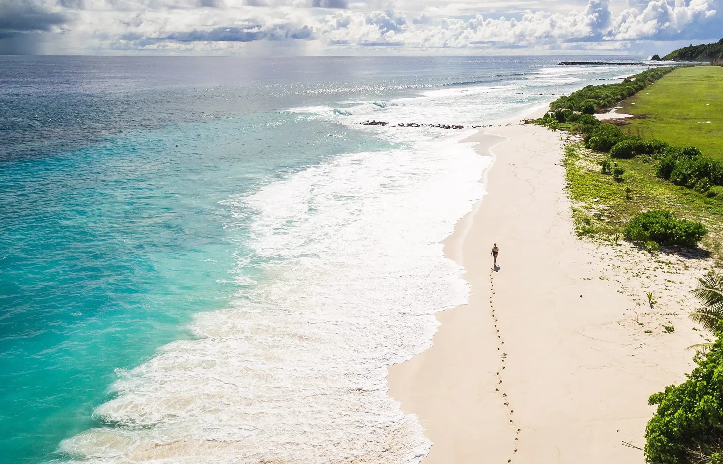 Guest walking along a long, empty white-sand beach beside turquoise surf at Fregate Island Private