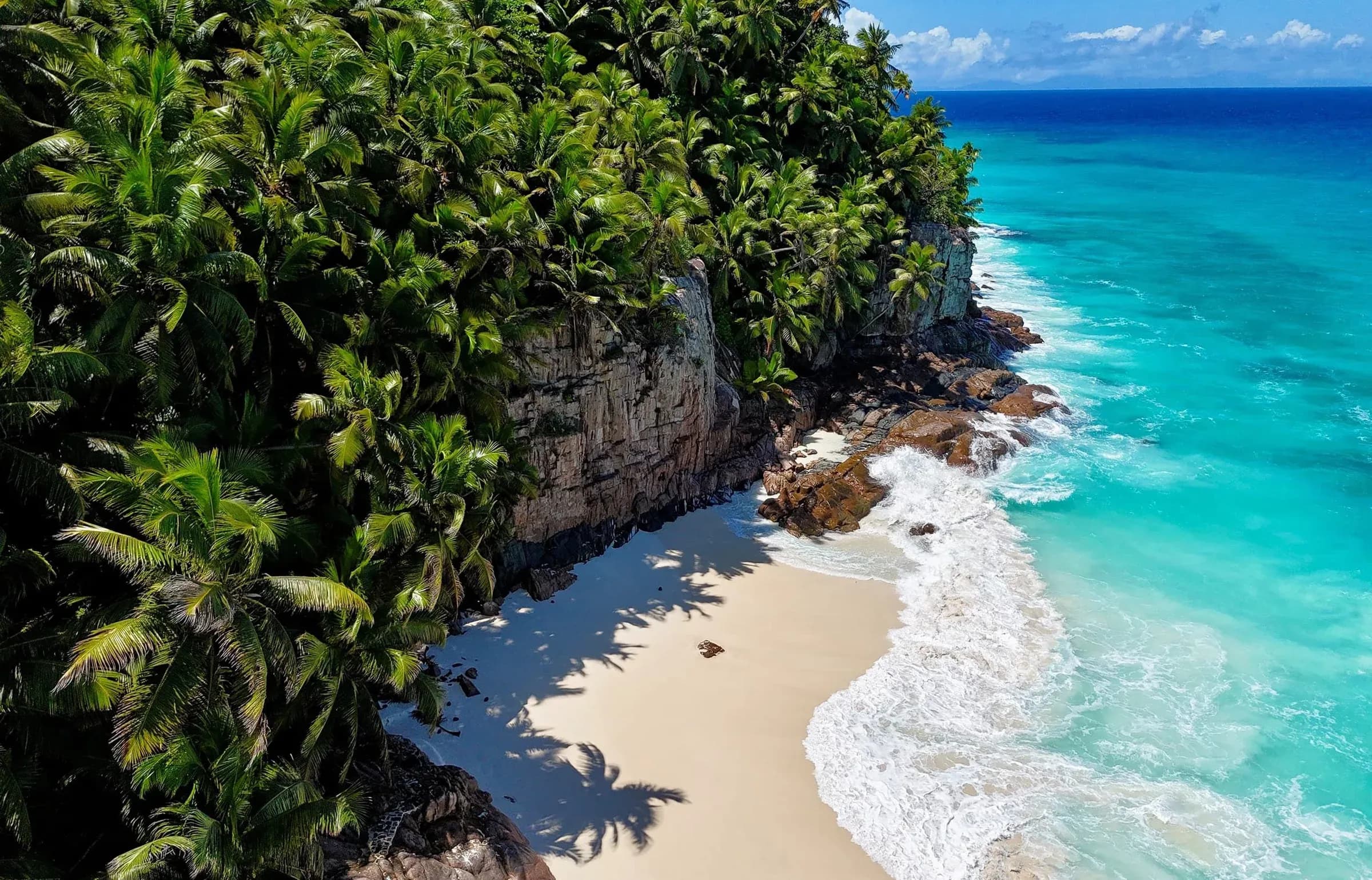 Secluded white-sand beach cove framed by granite boulders and palm forest at Fregate Island Private