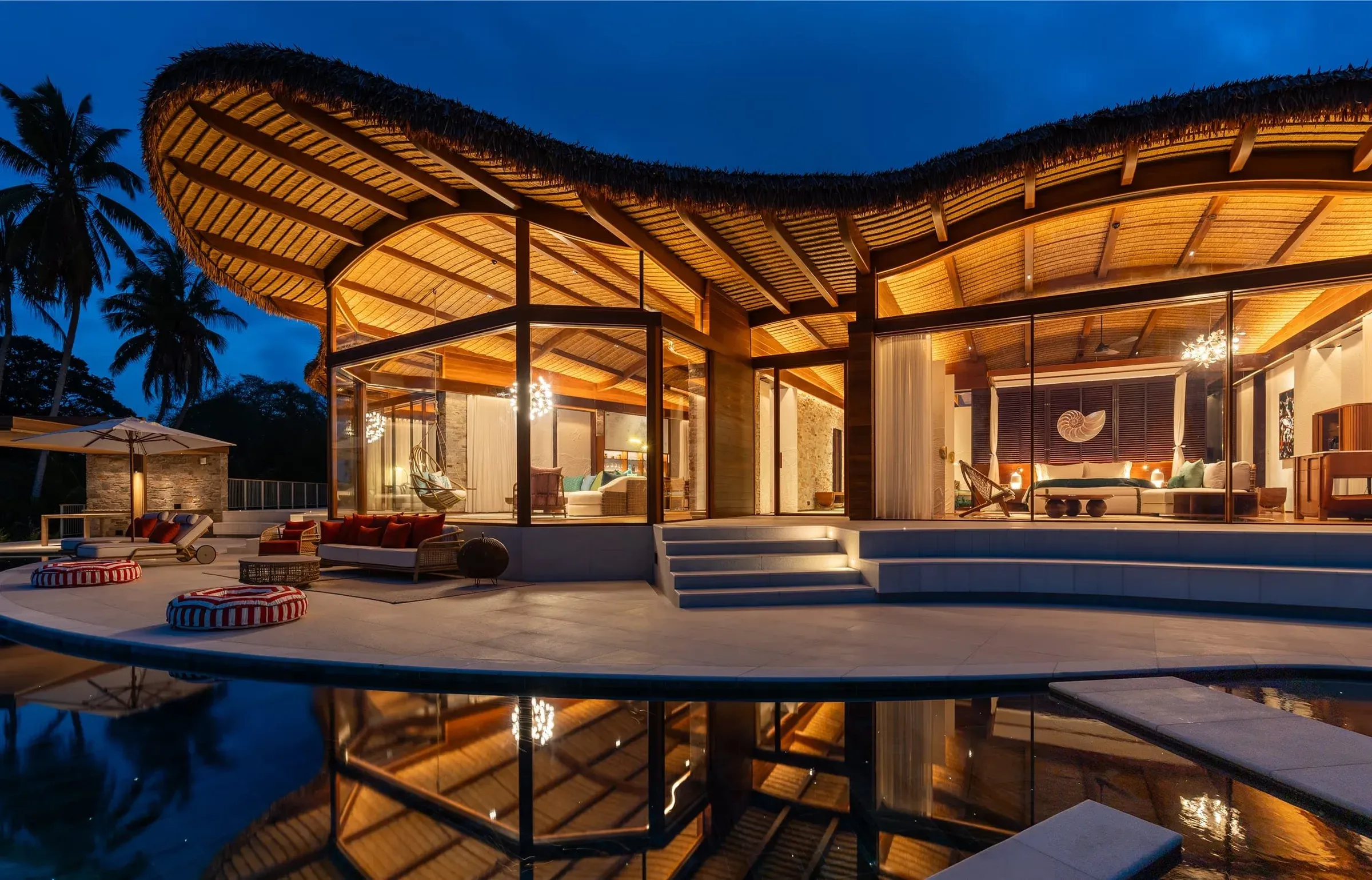 Curved timber-roofed Fregate Villa glowing at dusk, mirrored in its reflecting pool