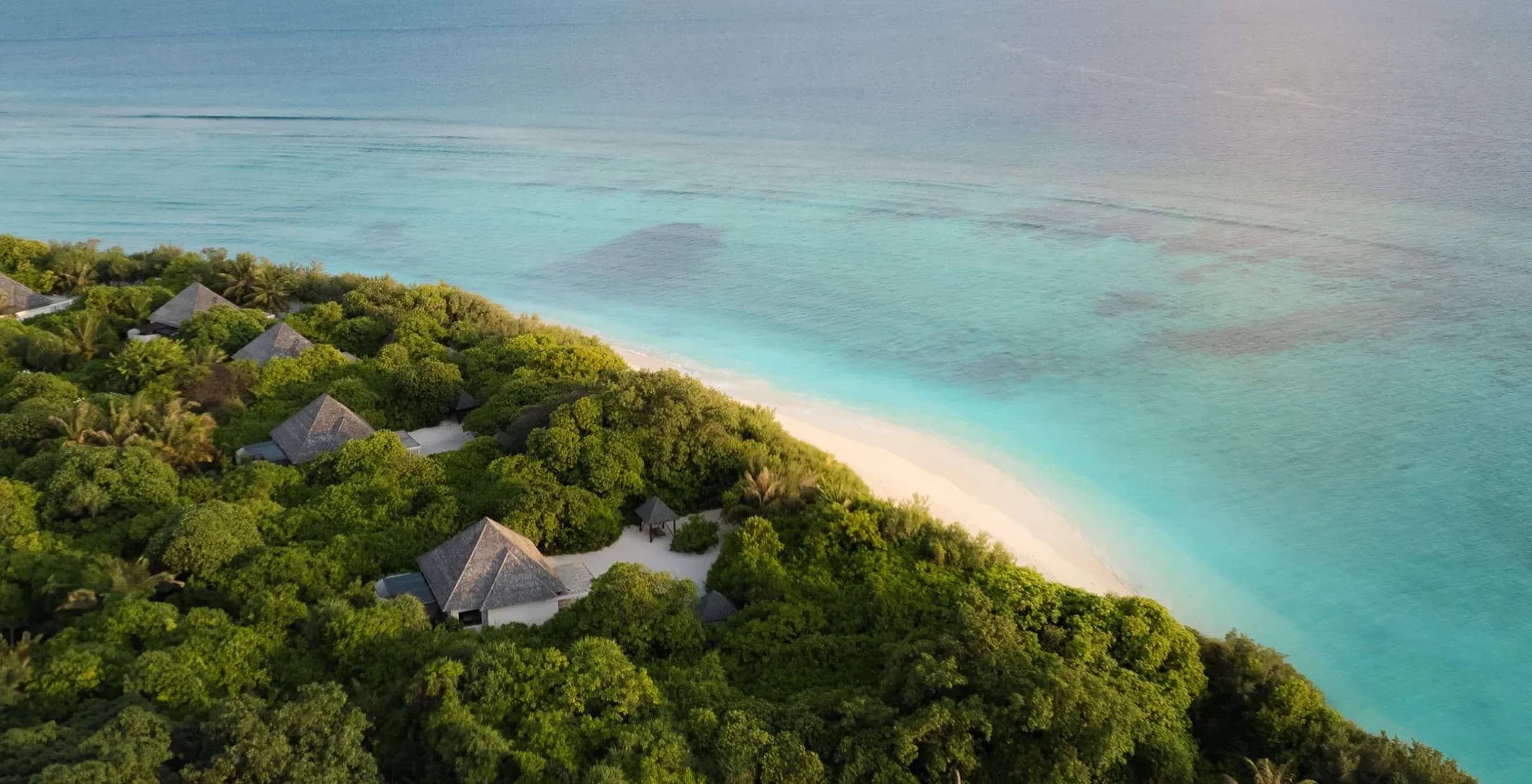 Aerial view of jungle-canopied beach villas and white sand at Hideaway Beach Resort & Spa, Haa Alifu Atoll