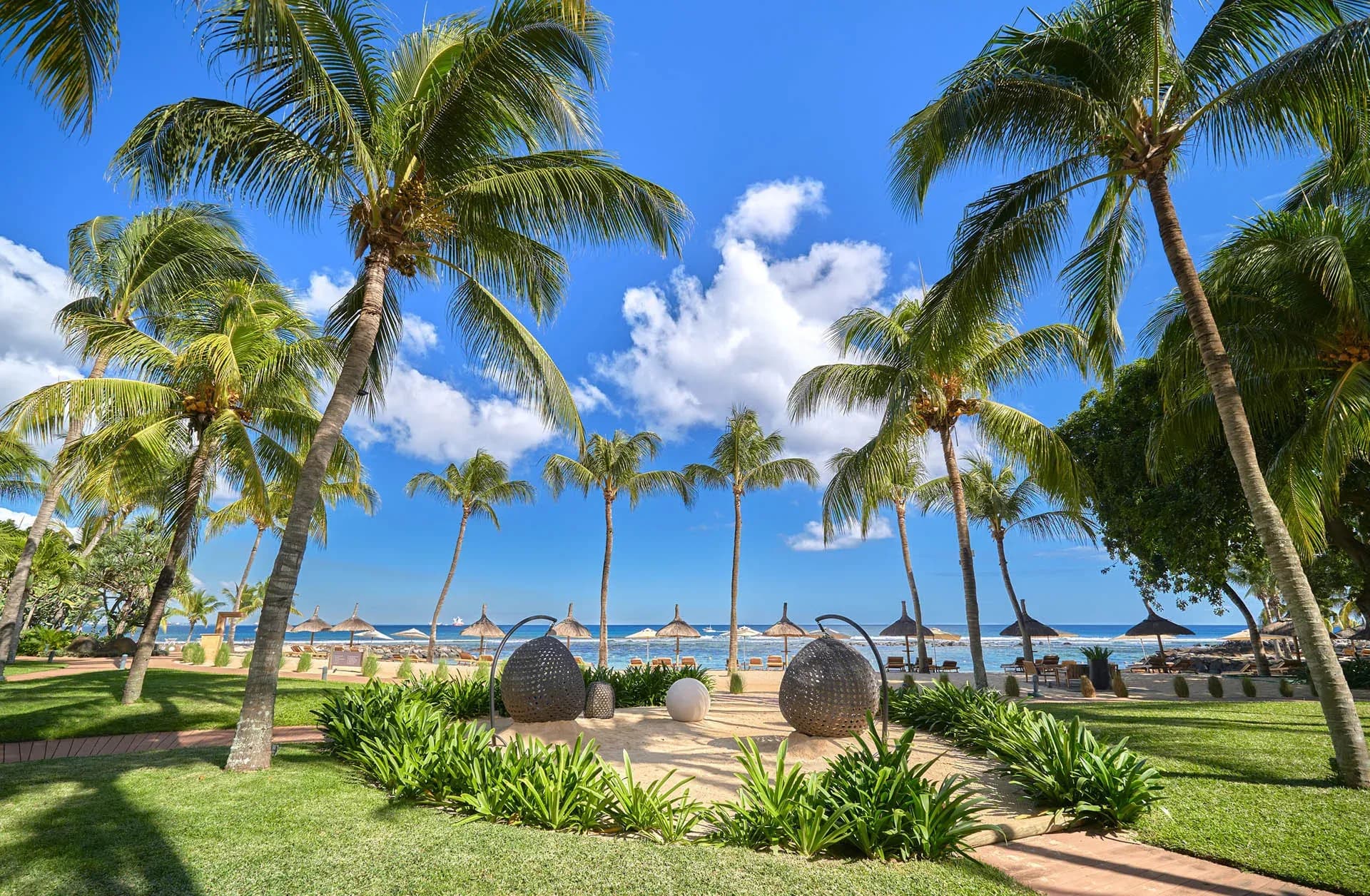 Palm-fringed beach with sculptural driftwood orbs on the sand at InterContinental Mauritius Resort Balaclava Fort