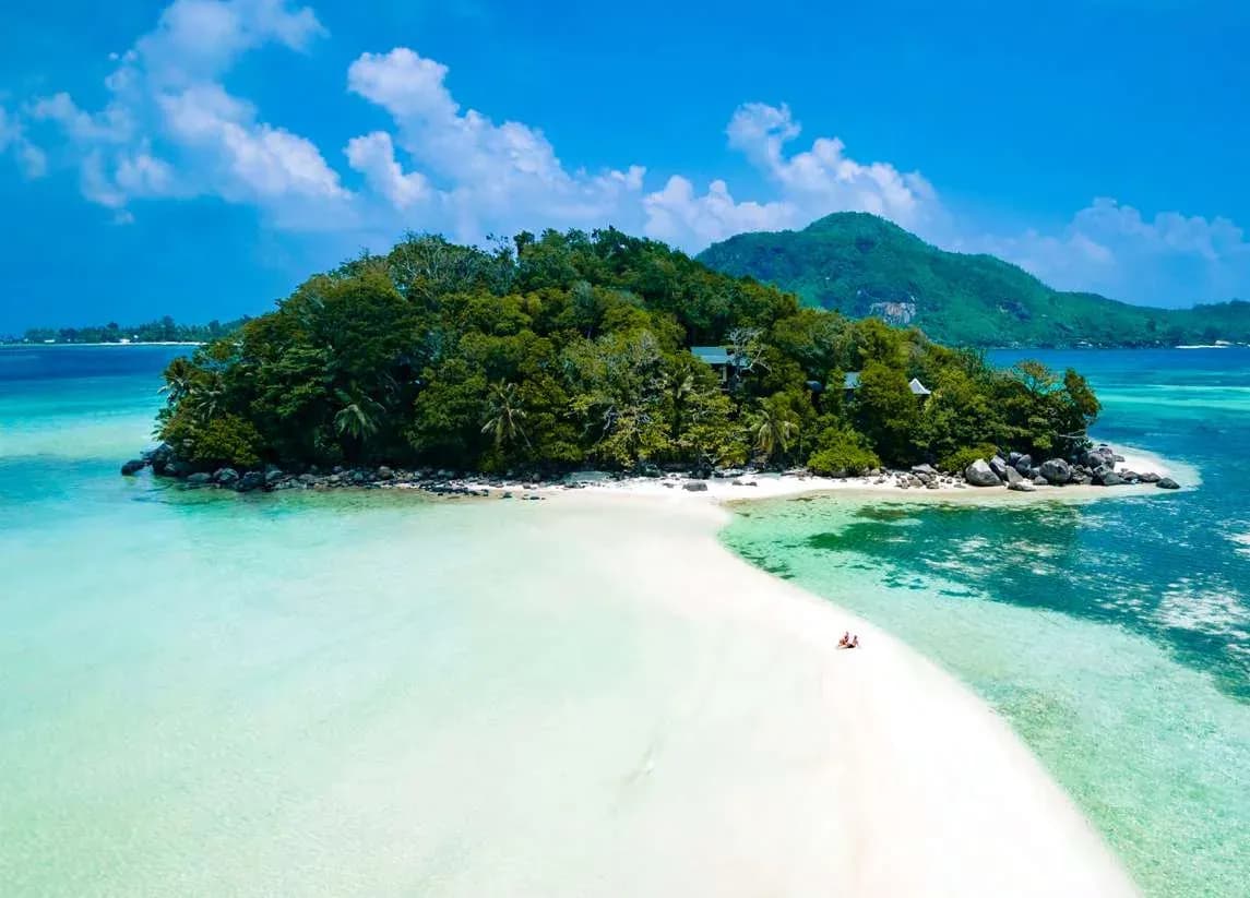 Aerial view of JA Enchanted Island Resort's private island, with villas among the trees and a white sandbar, Seychelles