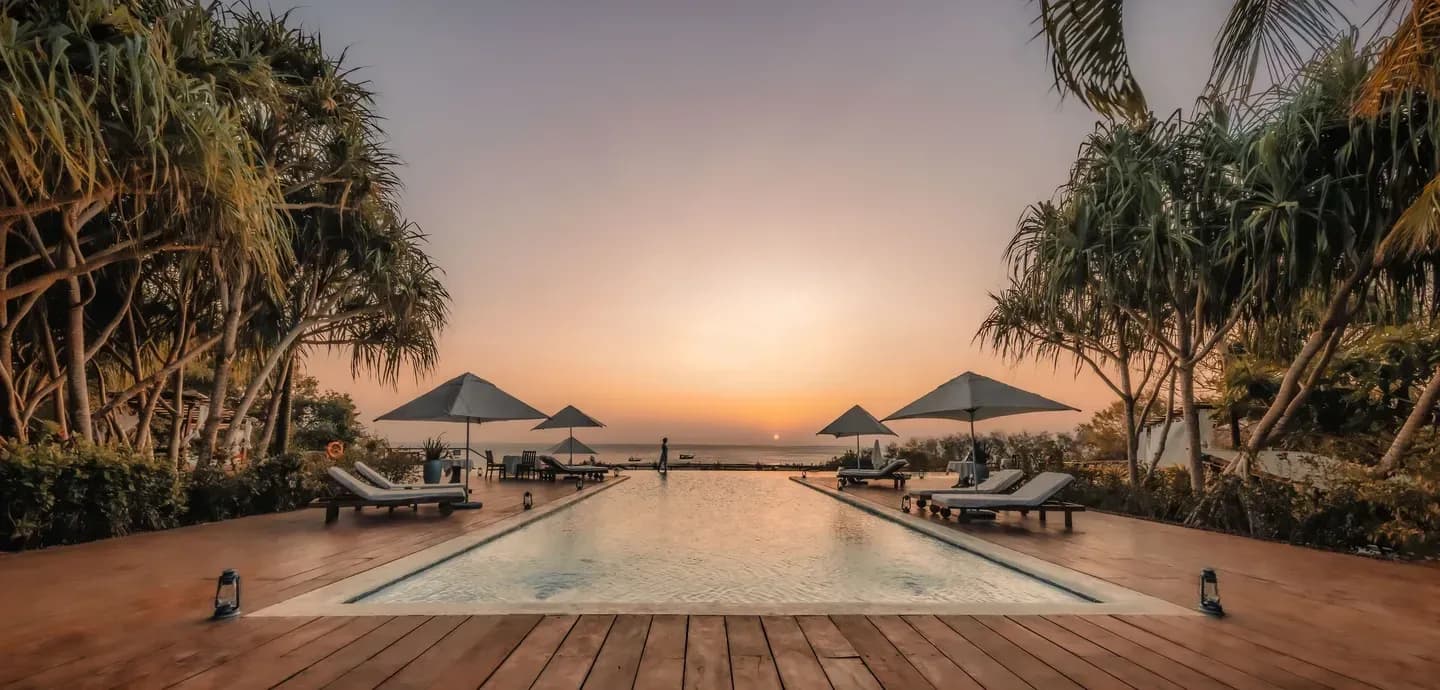 Kilindi Zanzibar's infinity pool at sunset, framed by palm trees looking out to the Indian Ocean