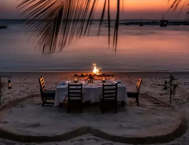 Candlelit beach dining table set on the sand at sunset for The Old Drift Restaurant and Bar, Kilindi Zanzibar