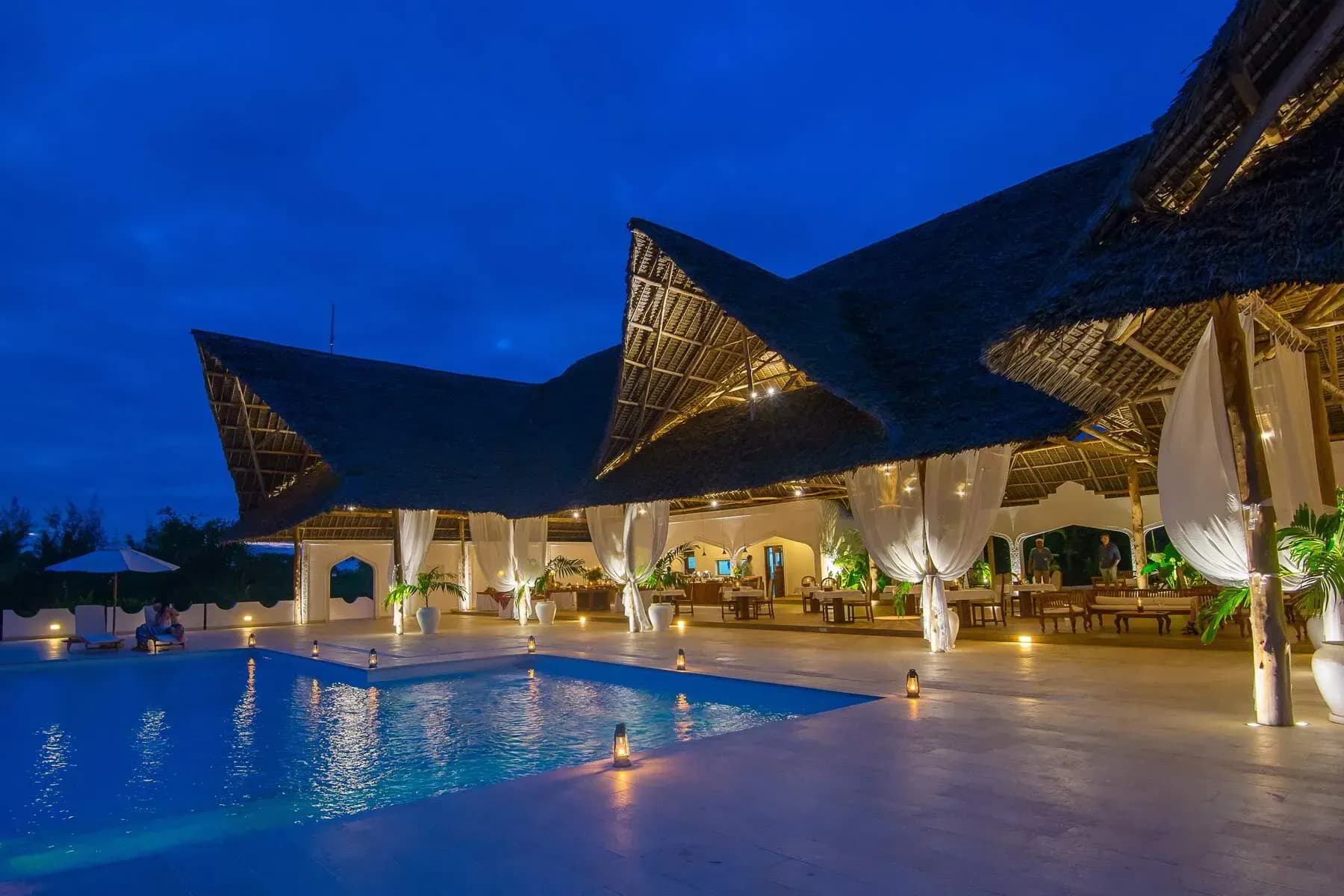 Konokono Main Restaurant's thatched dining pavilion lit at night beside the pool