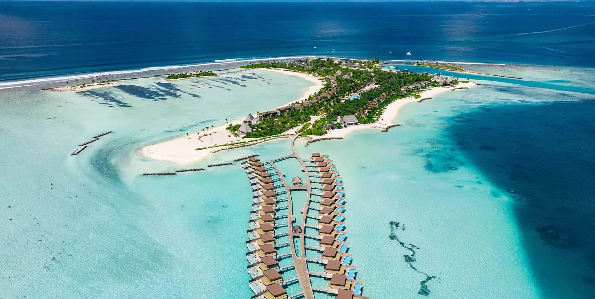 Aerial view of Kuda Villingili Resort Maldives showing the island and overwater villa jetty, North Malé Atoll