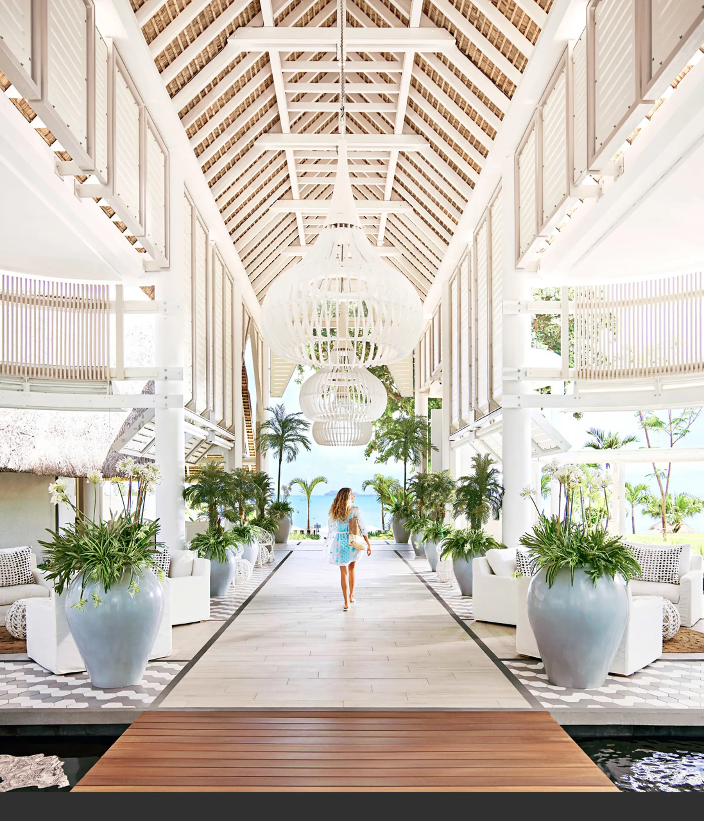 Timber walkway beneath white pavilion roofs leading to the beach at LUX* Grand Gaube