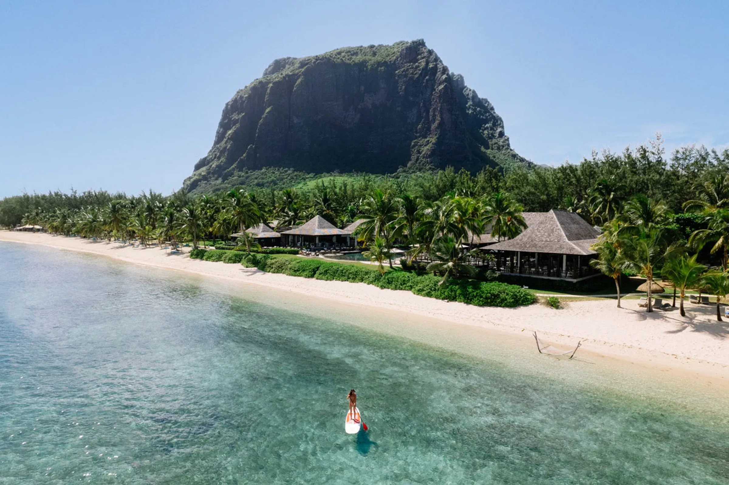 Aerial view of LUX* Le Morne Resort beach with Le Morne Brabant mountain behind and a paddleboarder in the lagoon, Mauritius