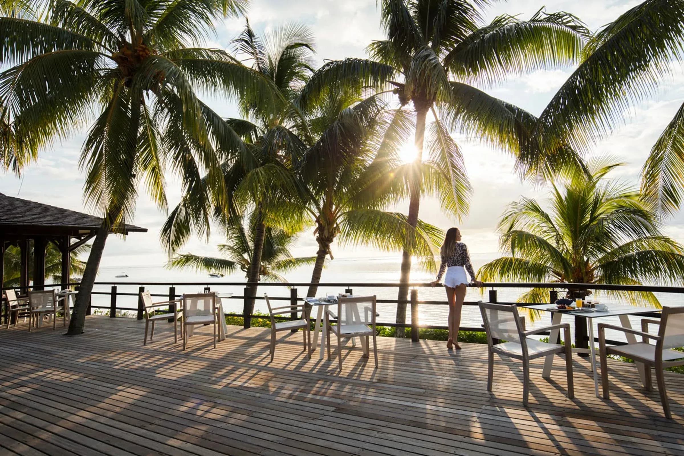Guest looking out over the lagoon from a palm-shaded terrace at sunset, LUX* Le Morne Resort