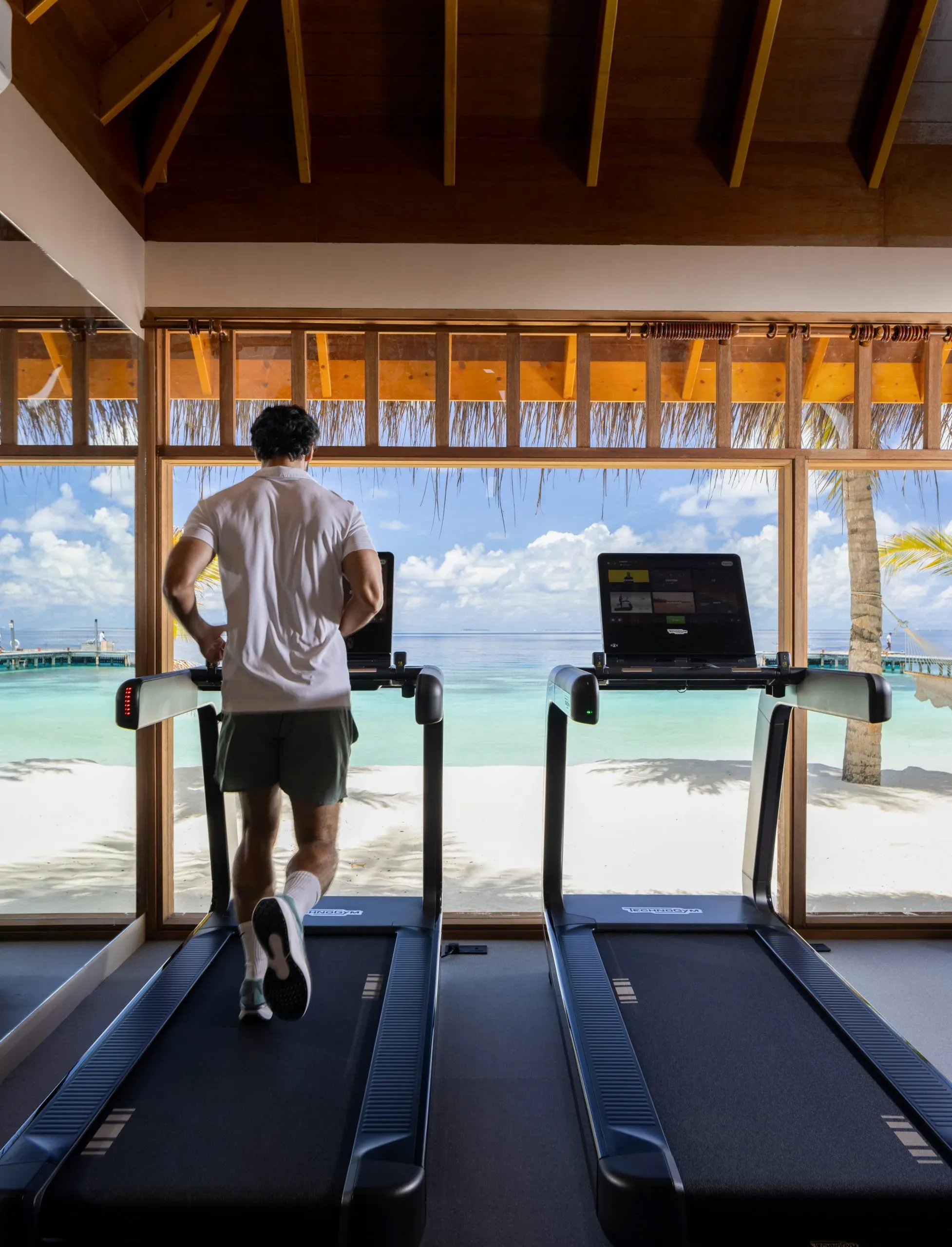 Guest running on a treadmill facing the lagoon at the Health & Fitness Centre, V Villas Maldives at Mirihi