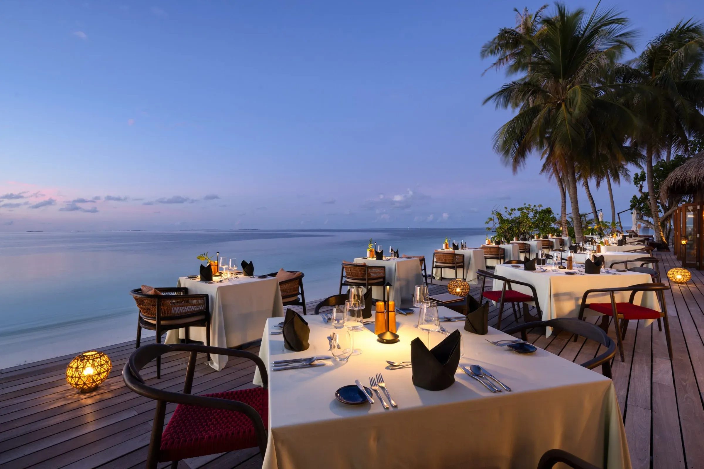 Beachfront dining tables set for dinner at dusk at Dhonveli restaurant, V Villas Maldives at Mirihi