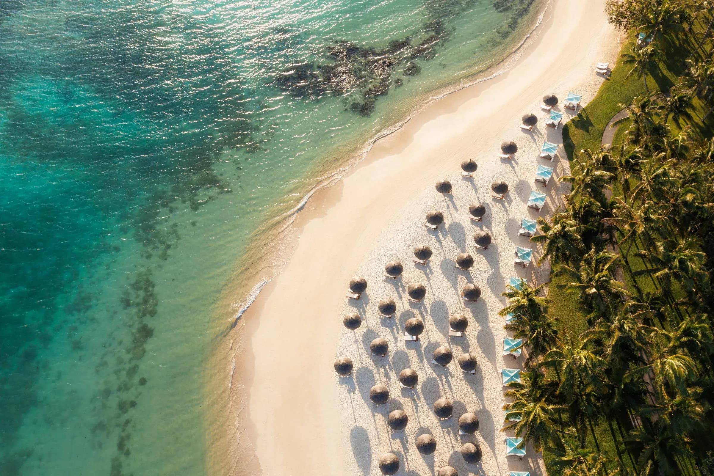 Aerial view of One&Only Le Saint Géran's beach with straw parasols and turquoise lagoon, Mauritius