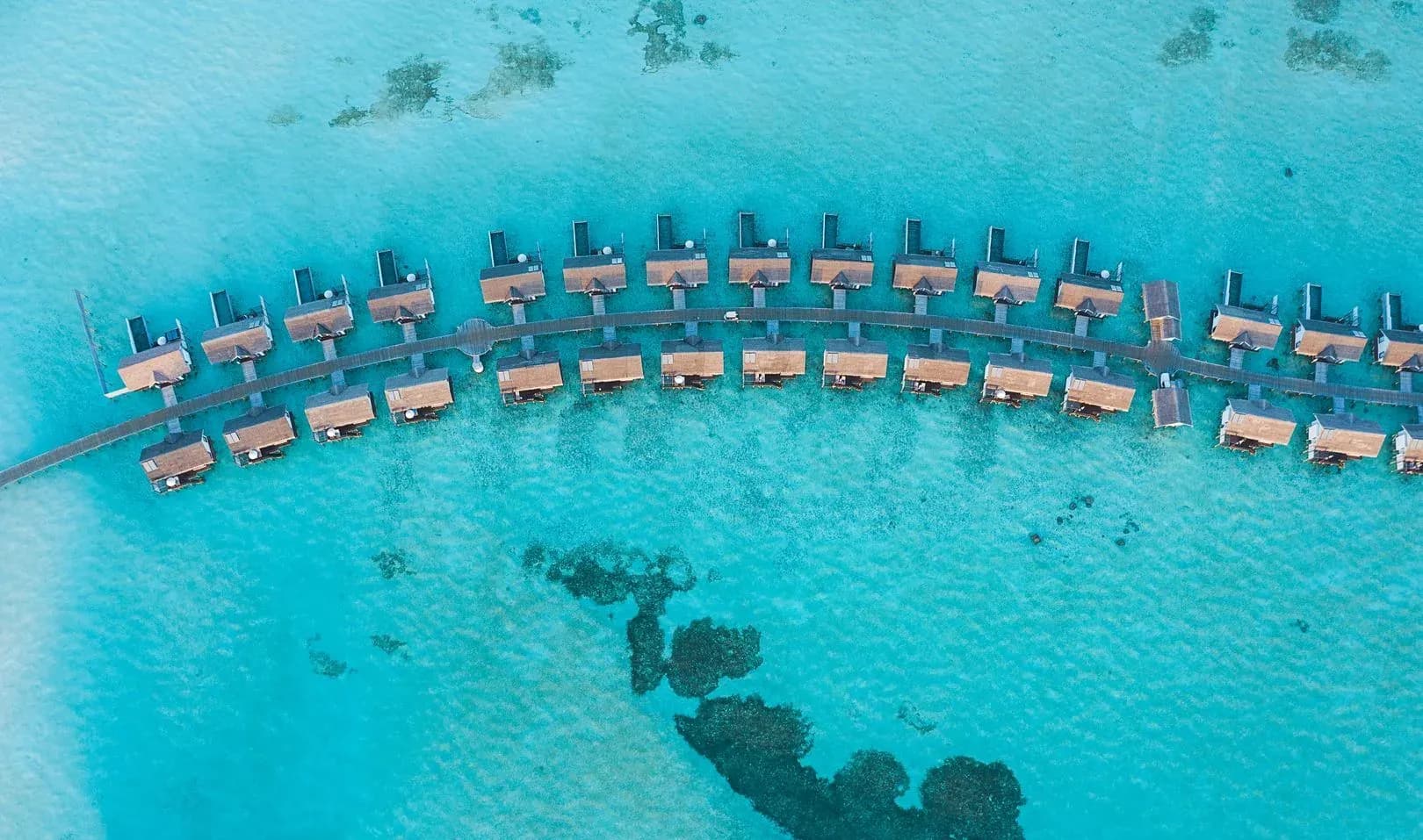 Aerial view of overwater villas in a curved arc over the turquoise lagoon at OZEN LIFE MAADHOO