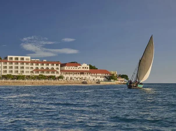 Park Hyatt Zanzibar seen from the water, with a traditional dhow sailing past the beachfront Mambo Msiige building, Stone Town