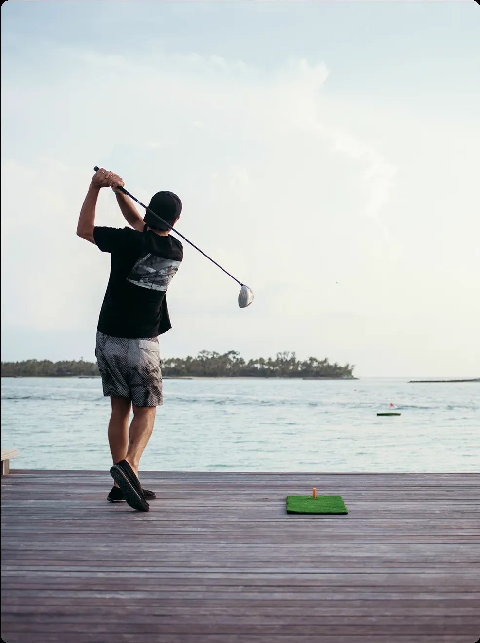 Guest teeing off over the lagoon at the floating golf deck, Patina Maldives