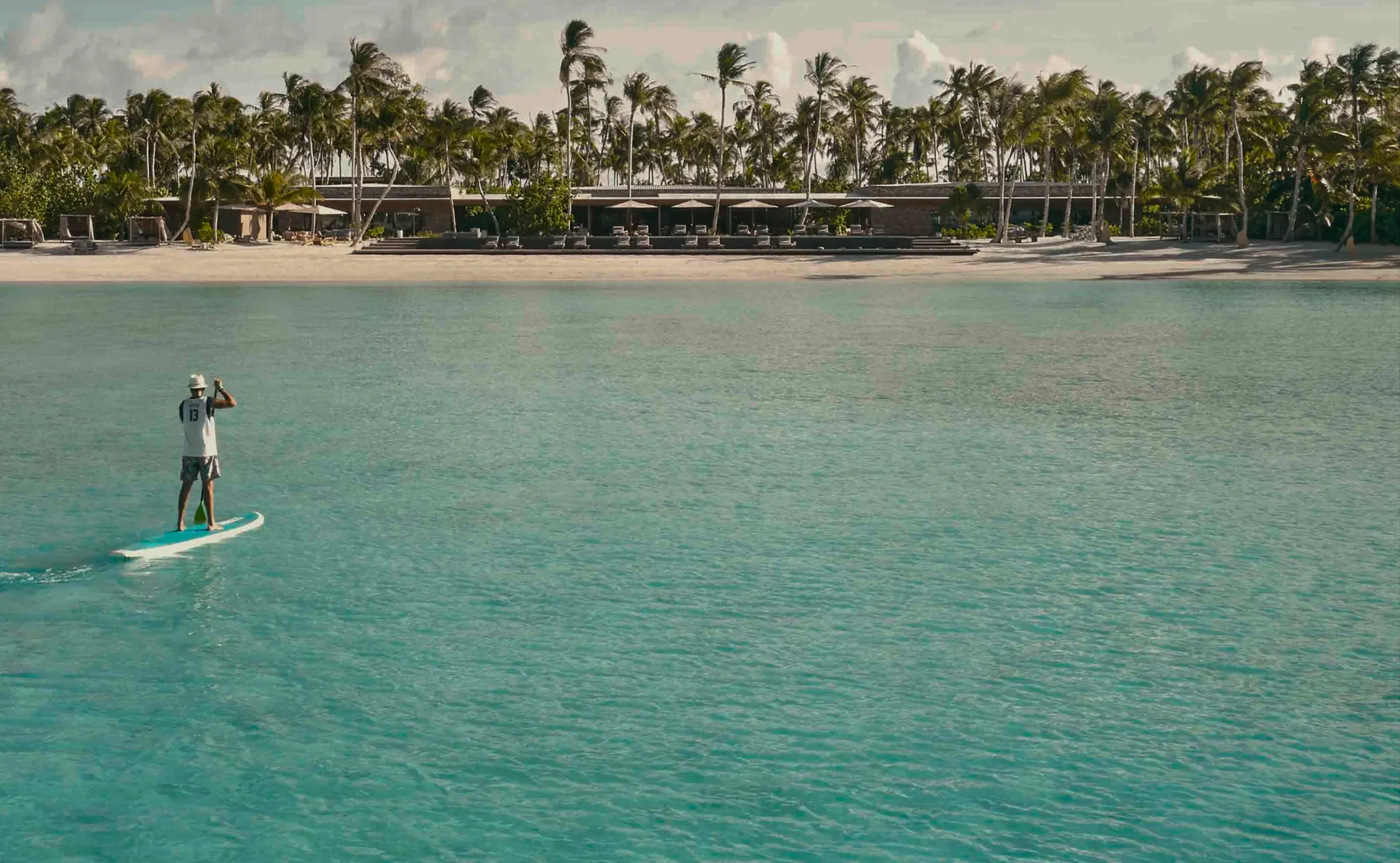 Guest paddleboarding in the lagoon in front of the resort, Patina Maldives Water Sports Centre