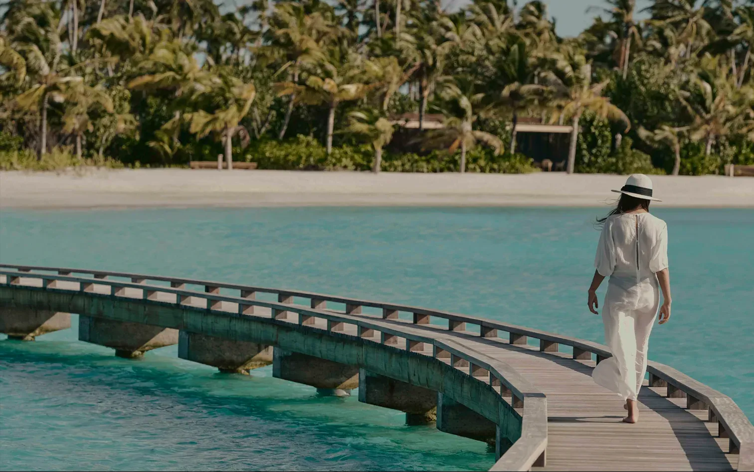 Guest walking a curved overwater boardwalk across the lagoon at Patina Maldives