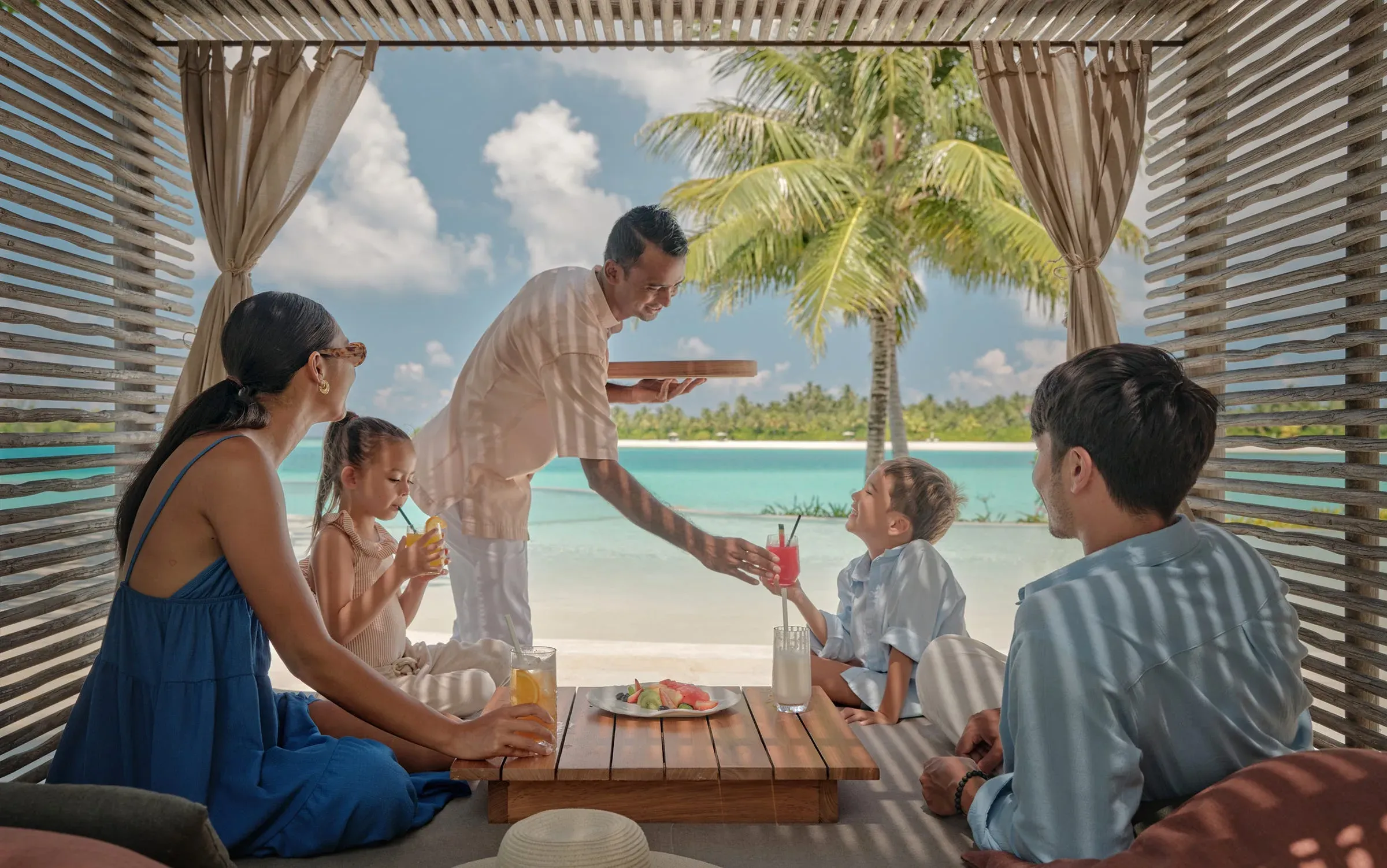 Family lounging beachside with turquoise ocean view at Fari Beach Club, Patina Maldives