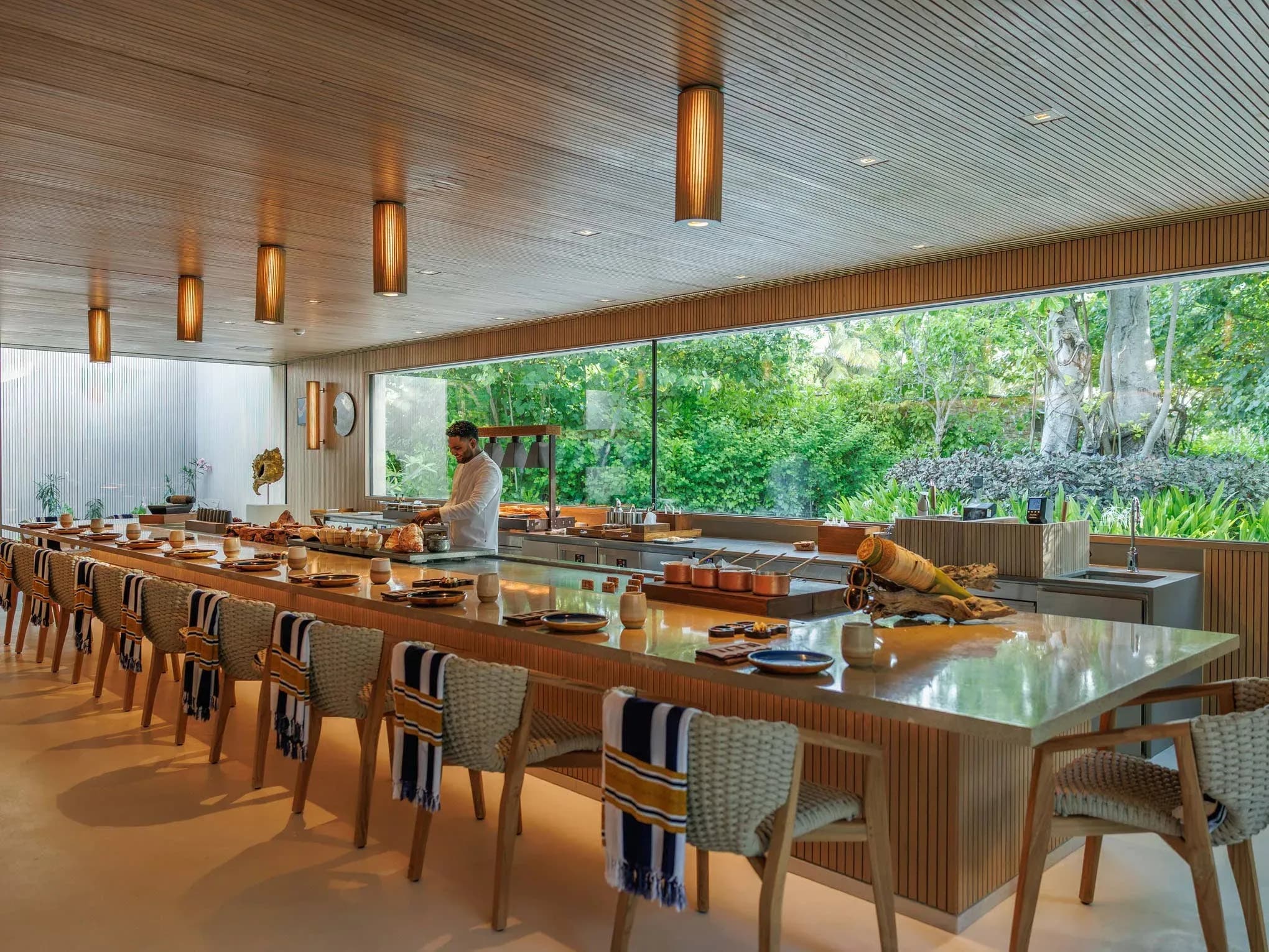 Illuminated modern dining structure of KANDU restaurant beneath palm trees, Patina Maldives