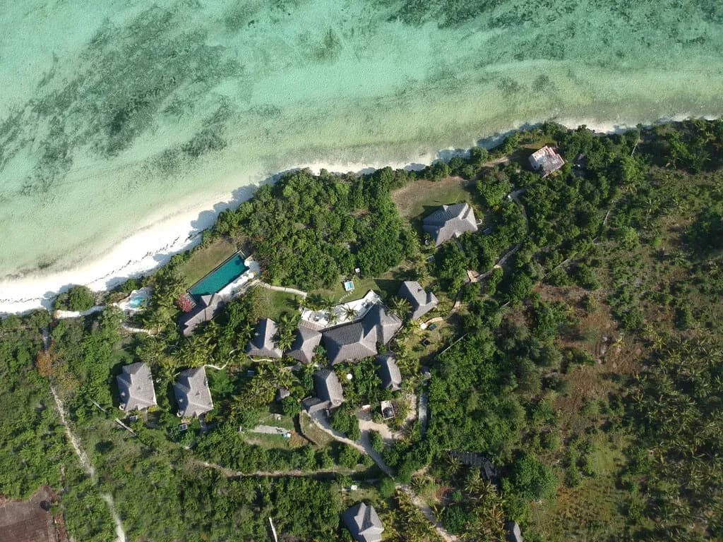 Aerial view of Qambani Luxury Resort on the Michamvi peninsula, showing thatched villas among palms above a turquoise lagoon, Zanzibar