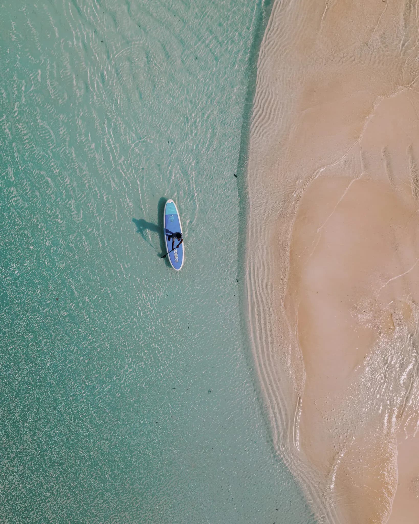 Guest stand-up paddleboarding across the clear lagoon at Soneva Jani