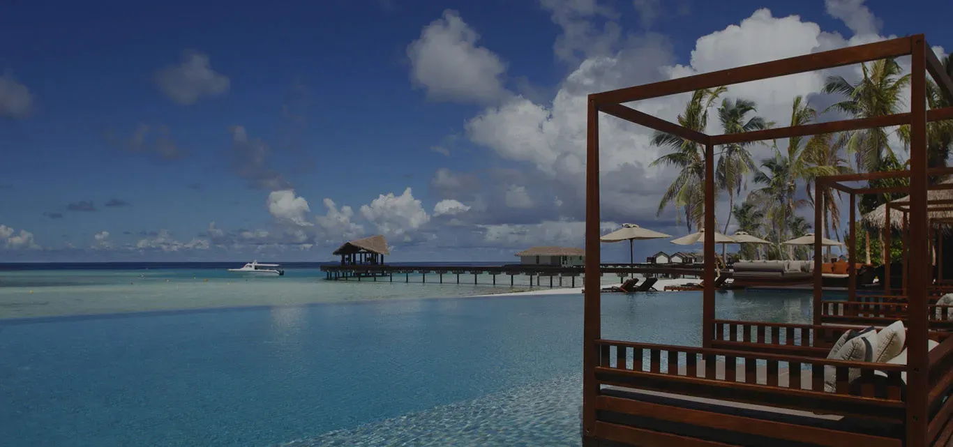 Beachfront infinity pool with cabanas and overwater villas in the distance, The Residence Maldives at Falhumaafushi