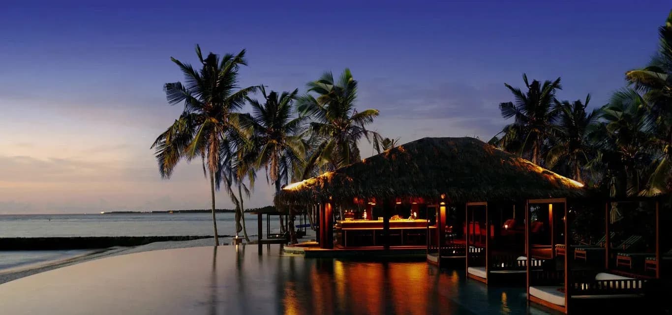 The Beach Bar pavilion lit at dusk beside the infinity pool, The Residence Maldives at Falhumaafushi