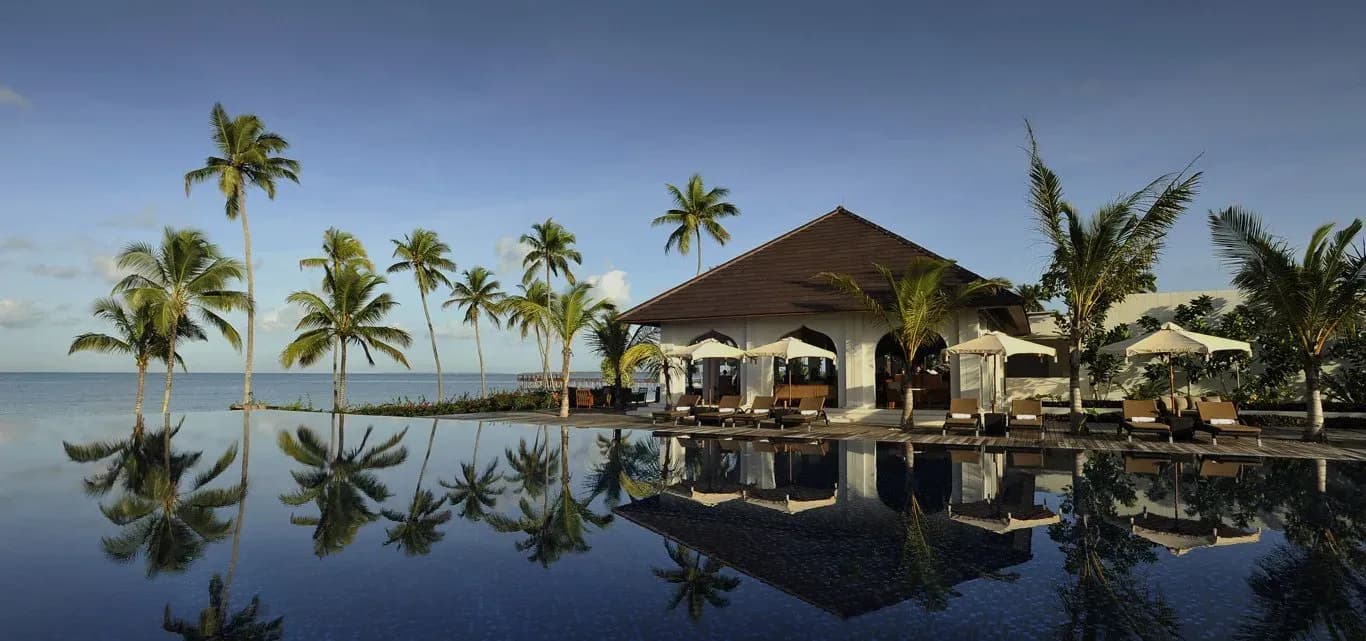 Infinity pool and beachfront pavilion at sunrise with reflected palm trees, The Residence Zanzibar