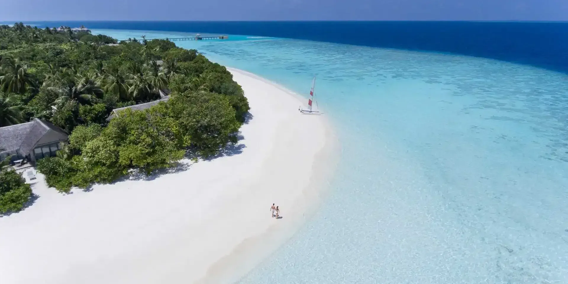 Aerial view of a couple walking the white-sand beach beside the turquoise lagoon at Vakkaru Maldives